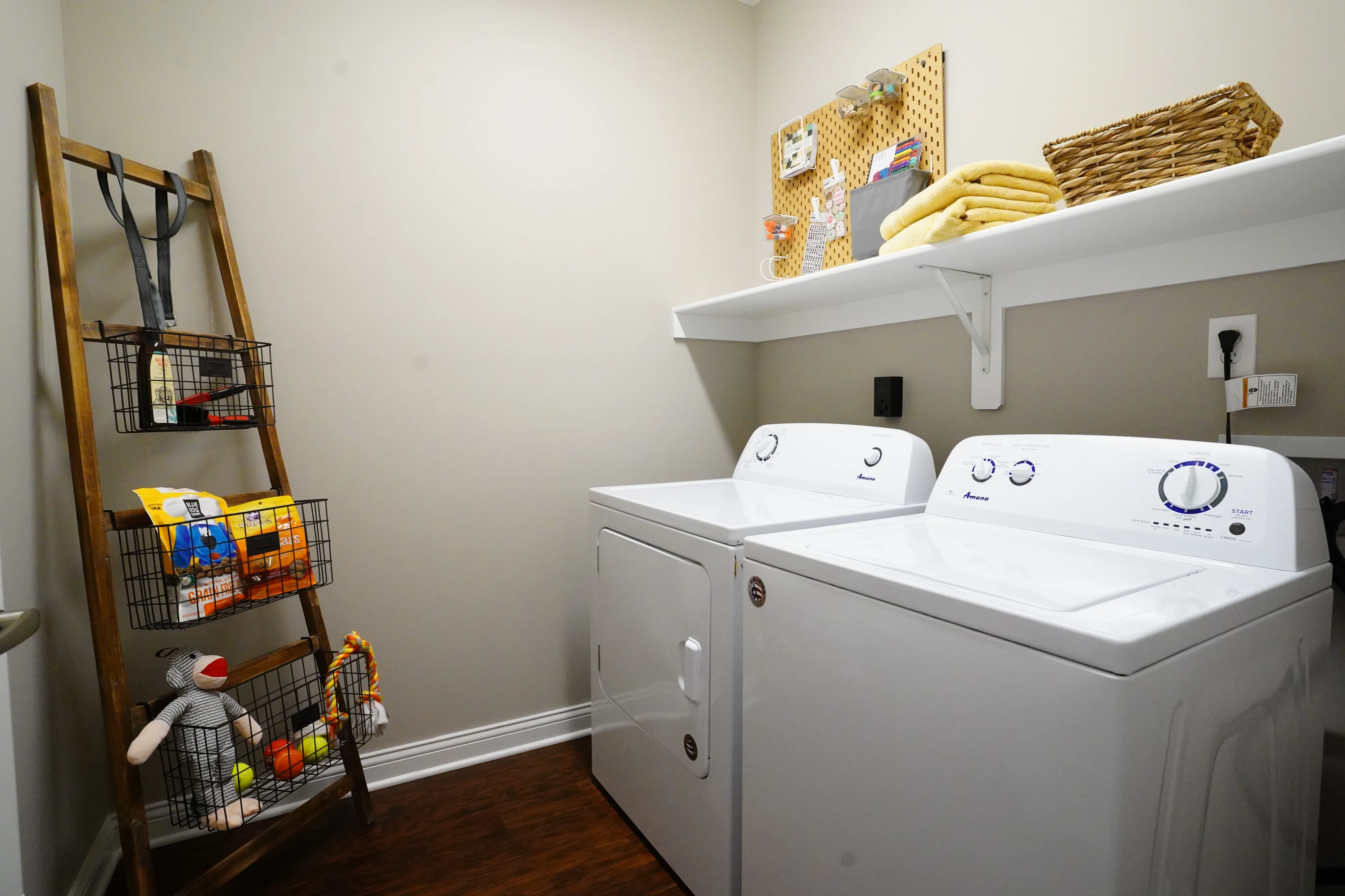 Charming laundry room featuring a sleek washer and dryer set, wooden ladder shelf with storage baskets, and a cozy organizational setup.