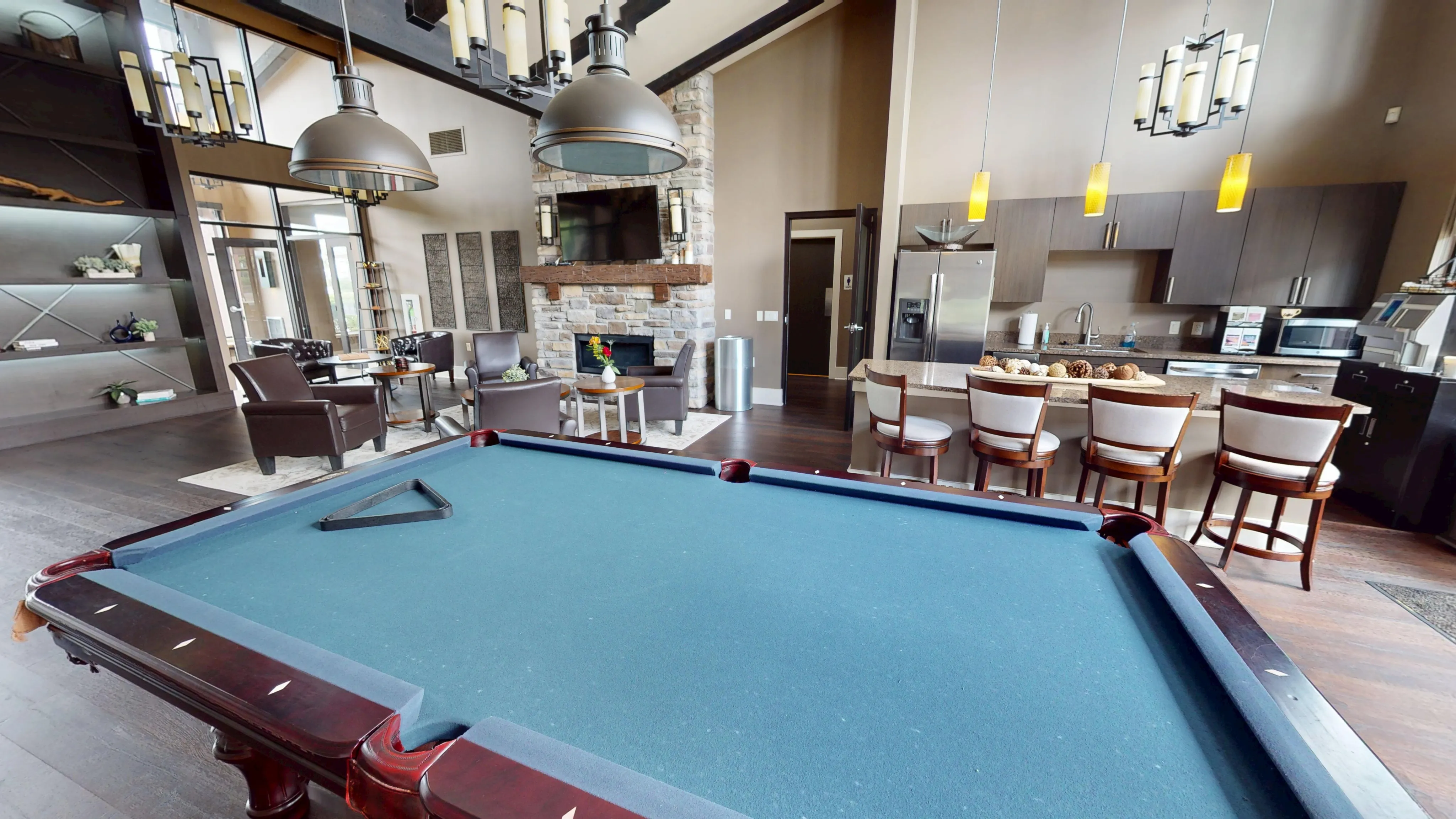 Luxurious open-concept living space featuring a stylish pool table, modern kitchen with bar seating, and a cozy seating area with a stone fireplace.