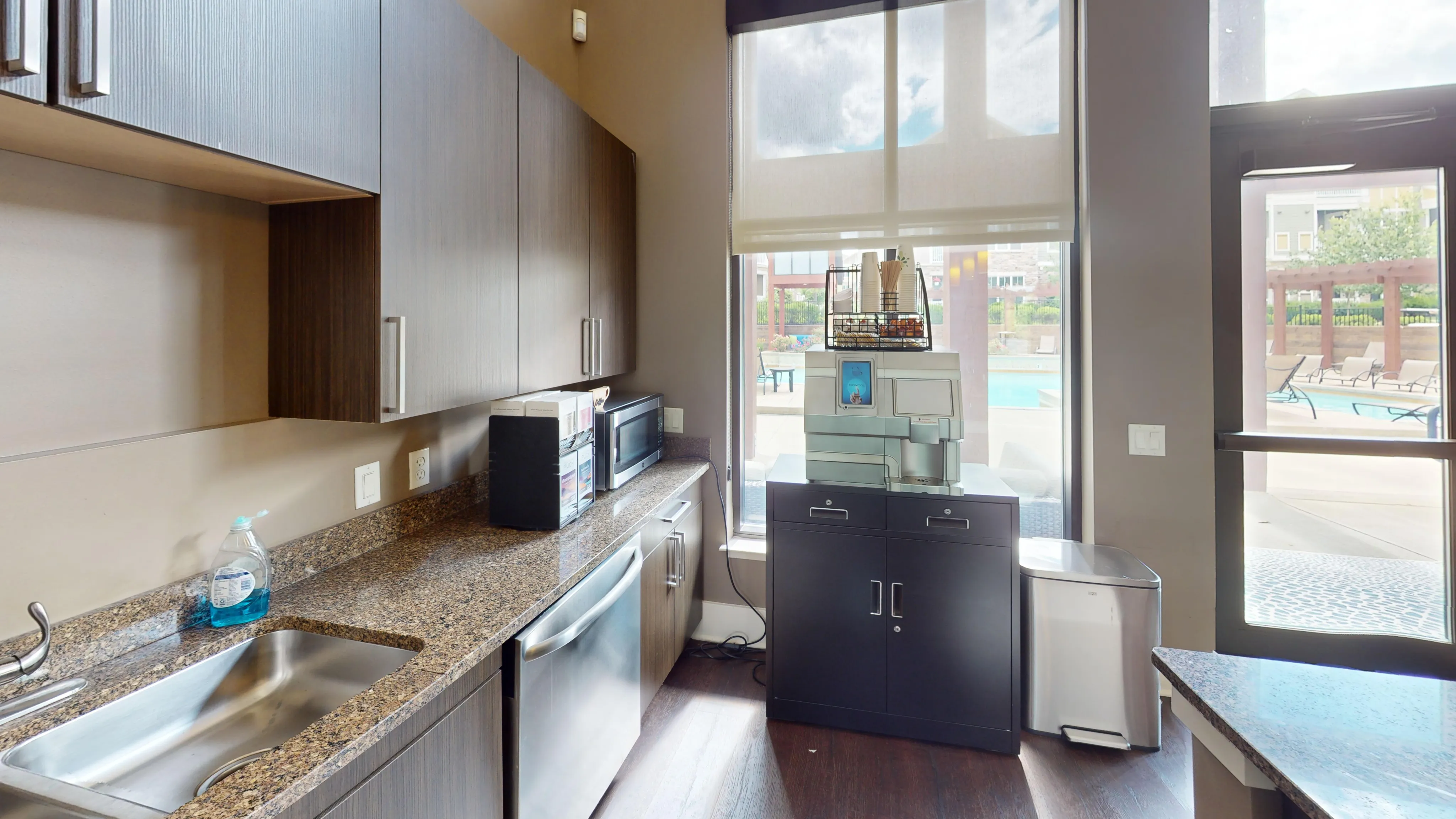 Modern kitchen with sleek cabinetry, granite countertops, and a view of the inviting outdoor pool area through large windows.