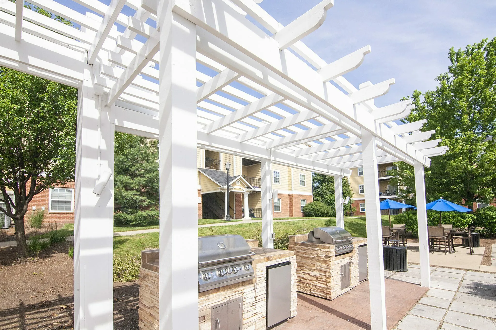 Inviting outdoor space with elegant white pergola and modern grill stations, complemented by surrounding greenery and patio seating.