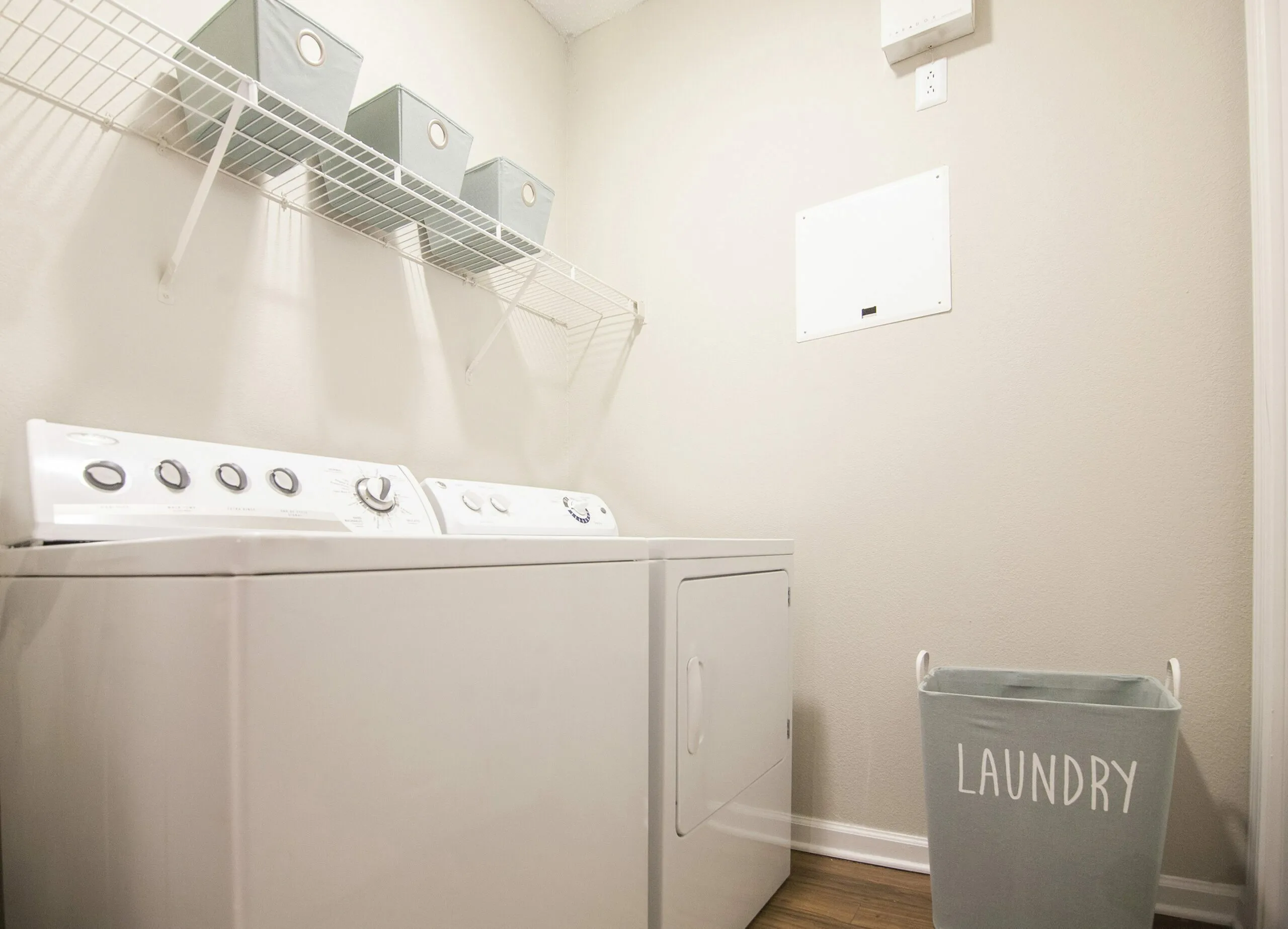 Contemporary laundry room with sleek white washer and dryer, organized storage bins, and a stylish laundry basket.