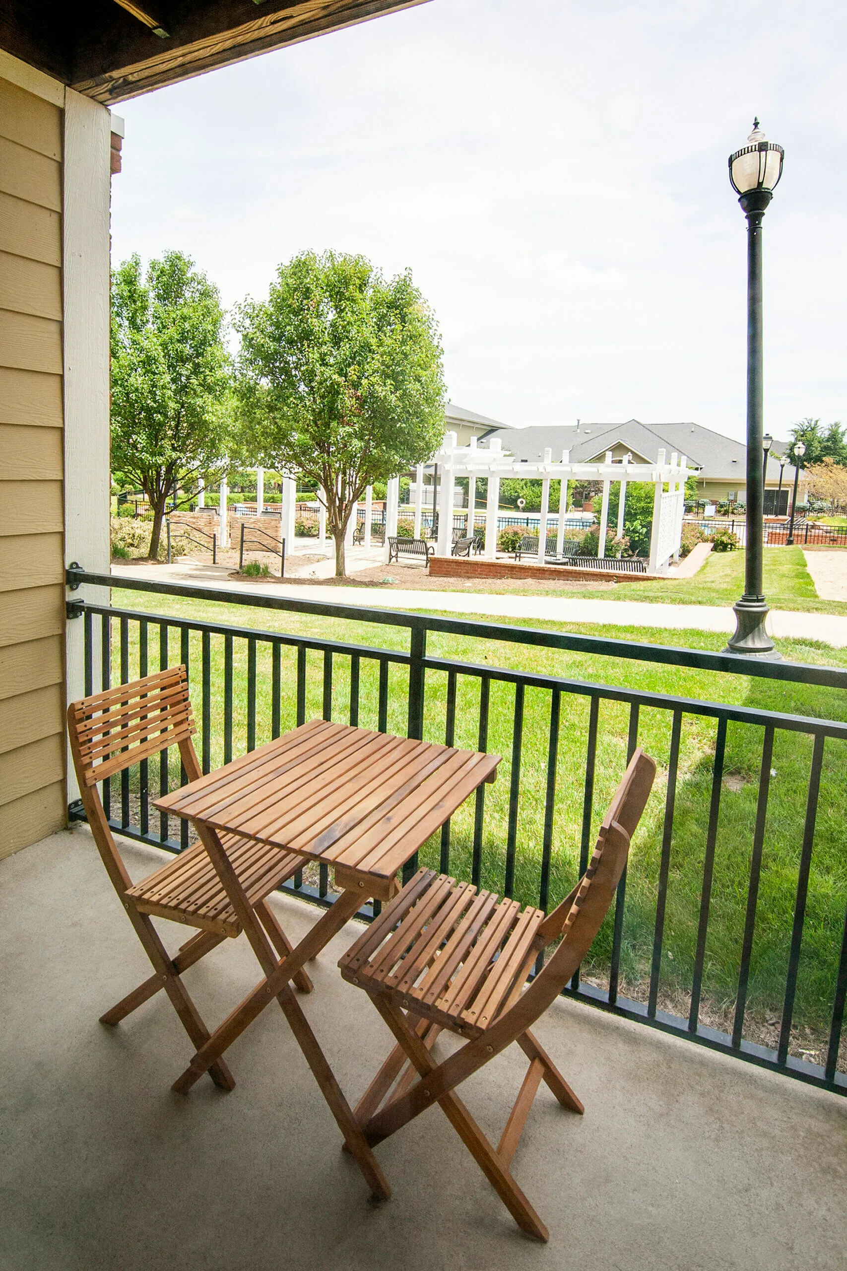 Charming balcony view featuring a cozy wooden bistro set, overlooking lush greenery and a serene outdoor pergola area.