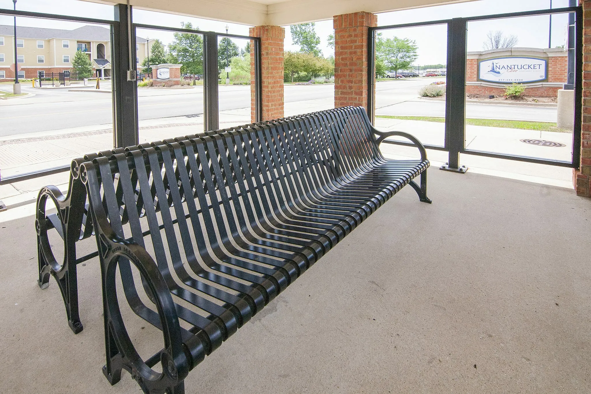 Inviting covered outdoor area with elegant metal bench offering a relaxing view of the vibrant community and lush greenery.