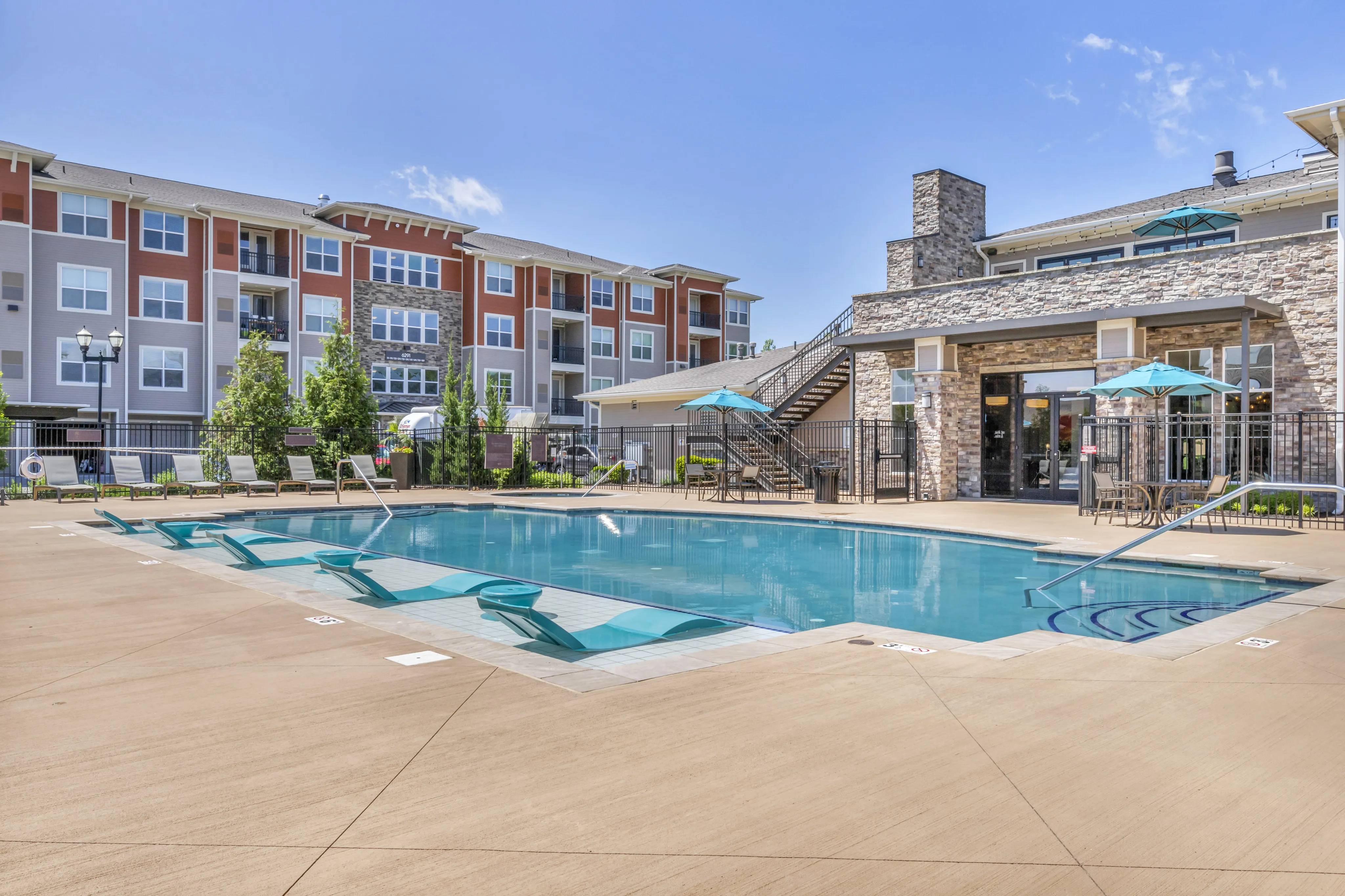 Luxurious apartment complex featuring a sparkling swimming pool, relaxing sun loungers, and modern architecture with stylish stone accents.