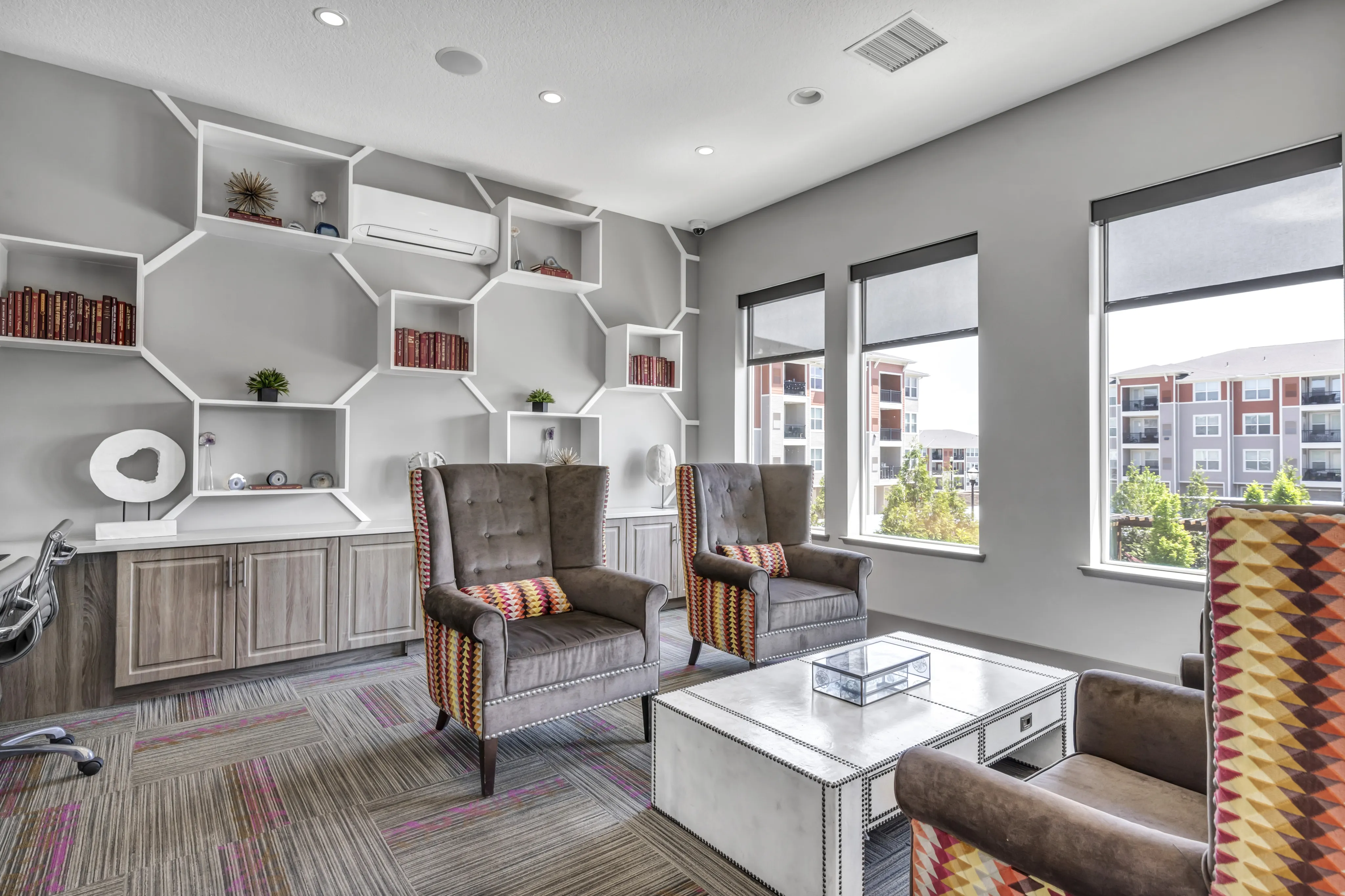 Bright, modern living area with unique geometric shelving, elegant armchairs, and large windows offering a scenic view.