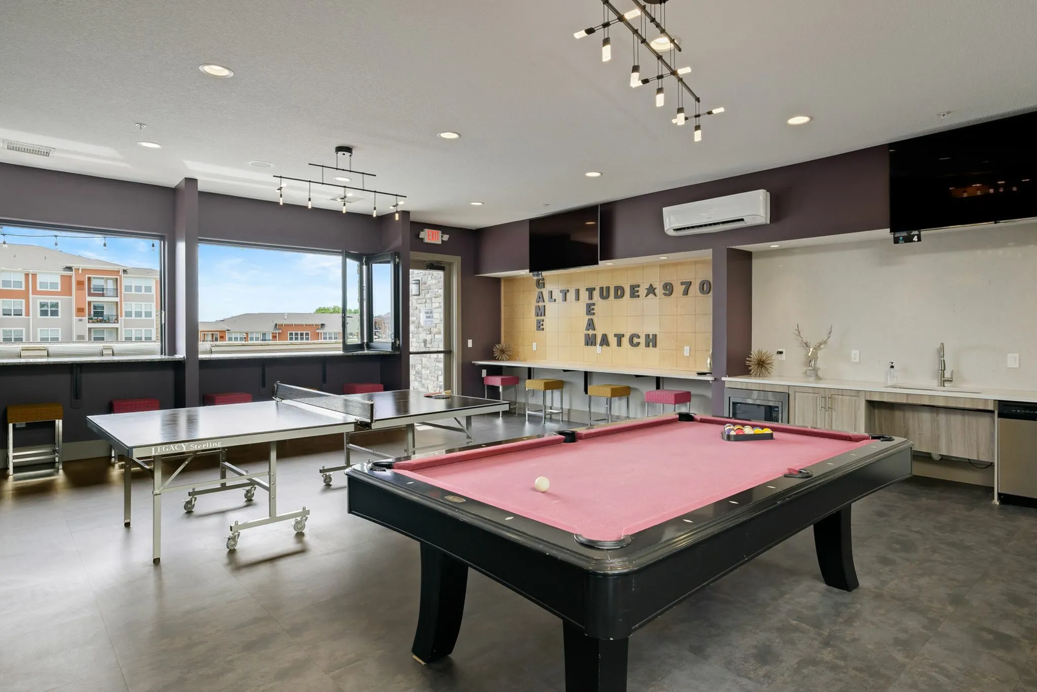 Luxurious community game room featuring a modern pool table, ping pong table, stylish bar seating, and expansive windows with scenic views.