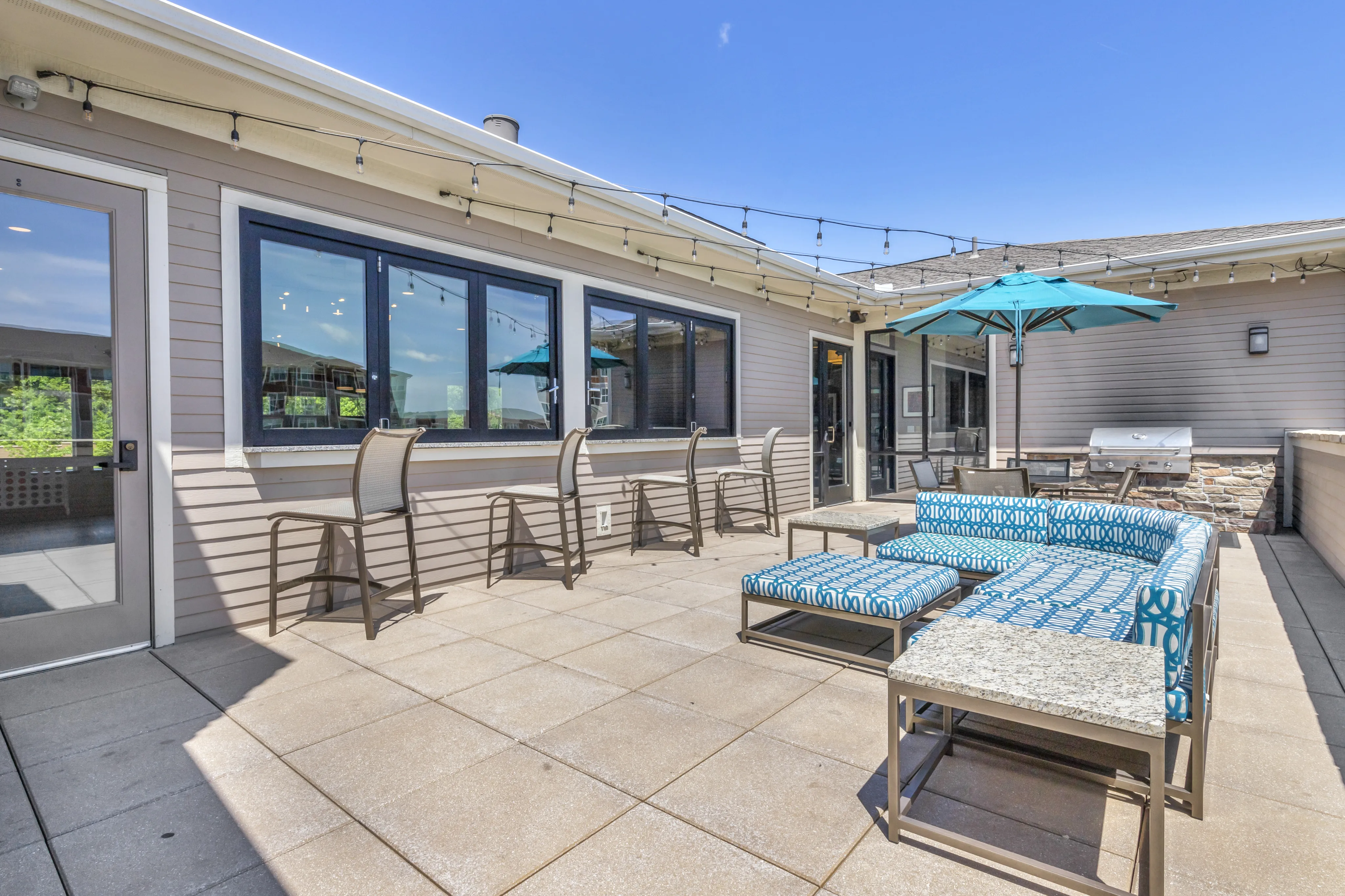Charming outdoor patio featuring stylish seating, a vibrant blue umbrella, and string lights for a perfect relaxation spot.