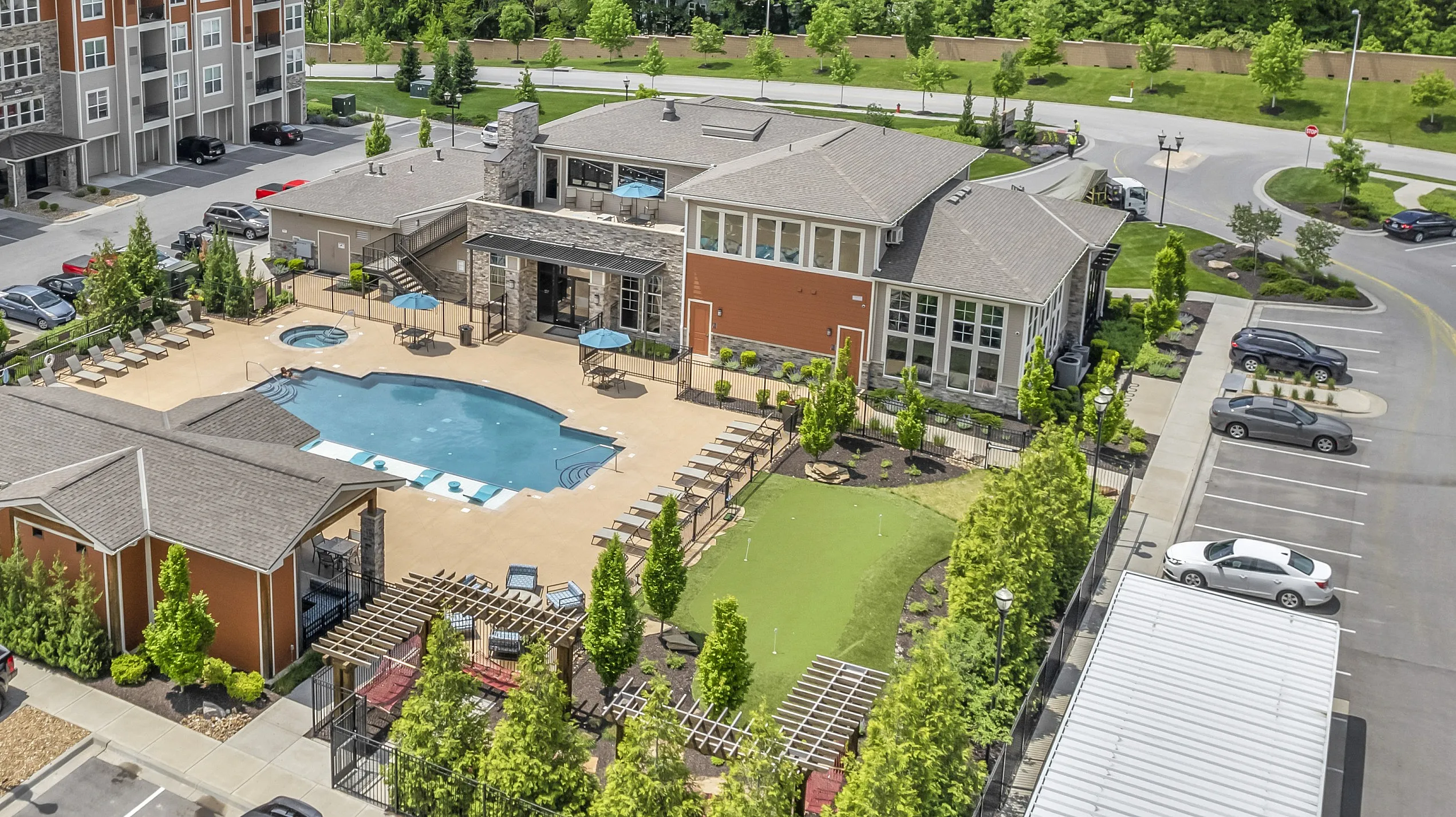 Aerial view of a modern apartment complex with spacious balconies, a large swimming pool, and lush green surroundings.