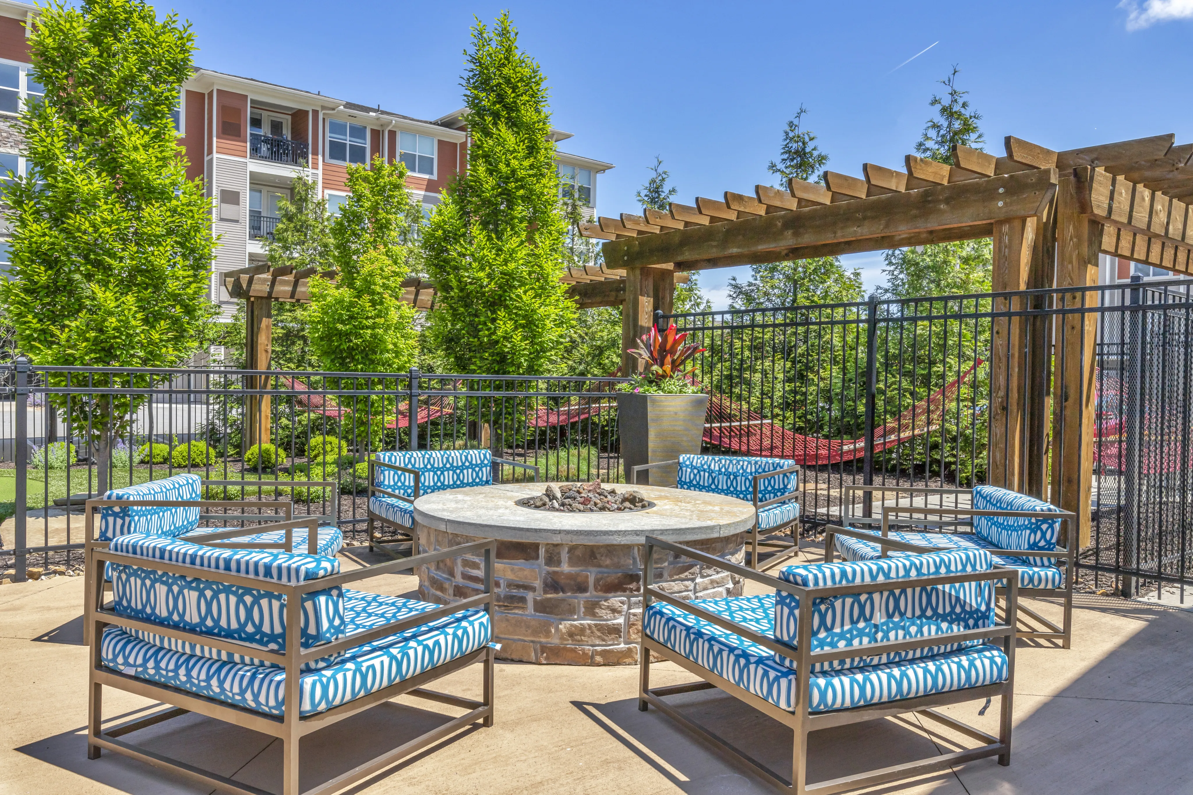 Inviting outdoor lounge area featuring stylish seating around a stone fire pit, under a wooden pergola, perfect for relaxation and social gatherings.