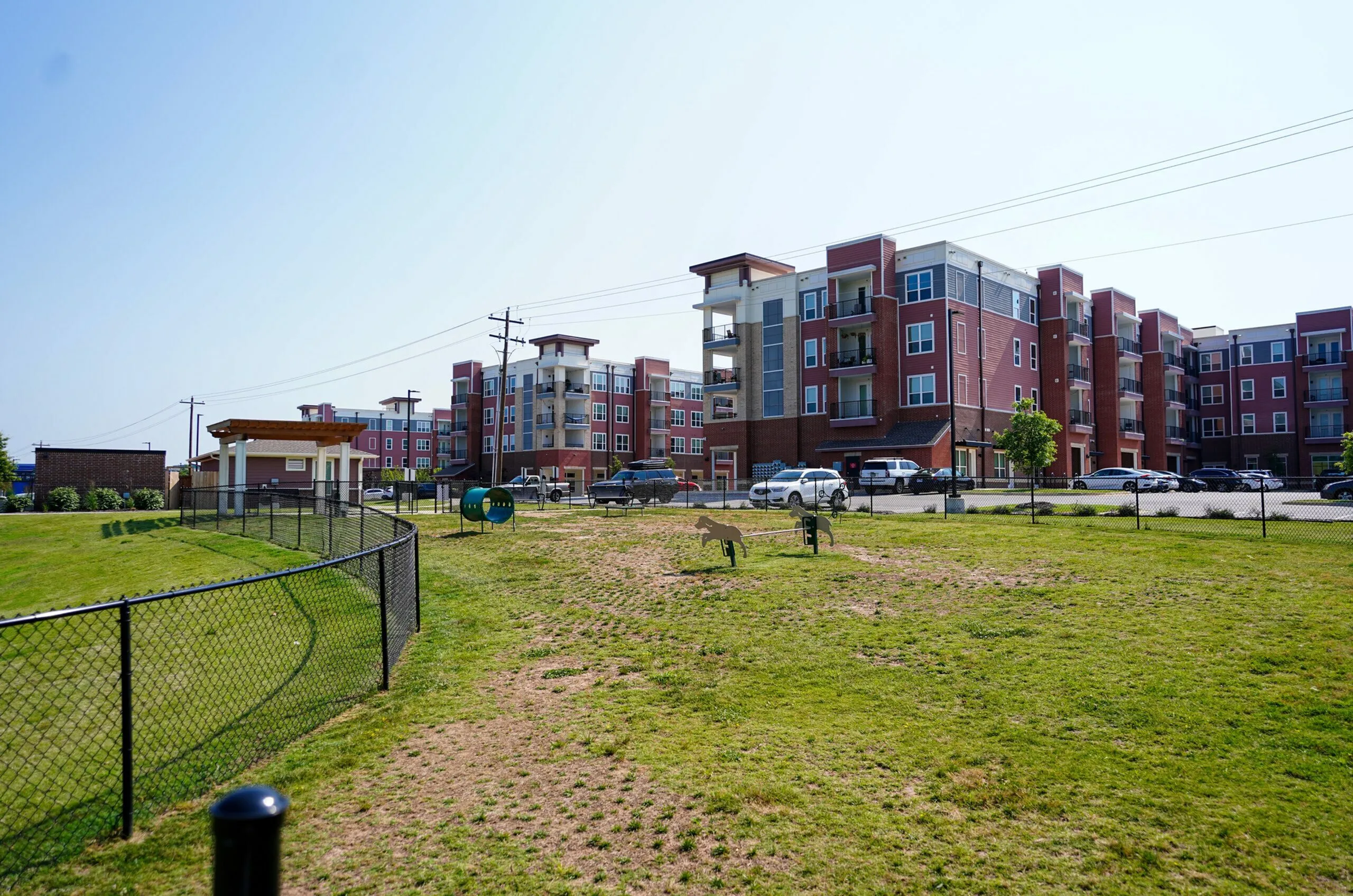 Modern apartment complex with vibrant red brick facade, surrounded by lush green lawns and ample parking space, offering a blend of urban convenience and greenery.