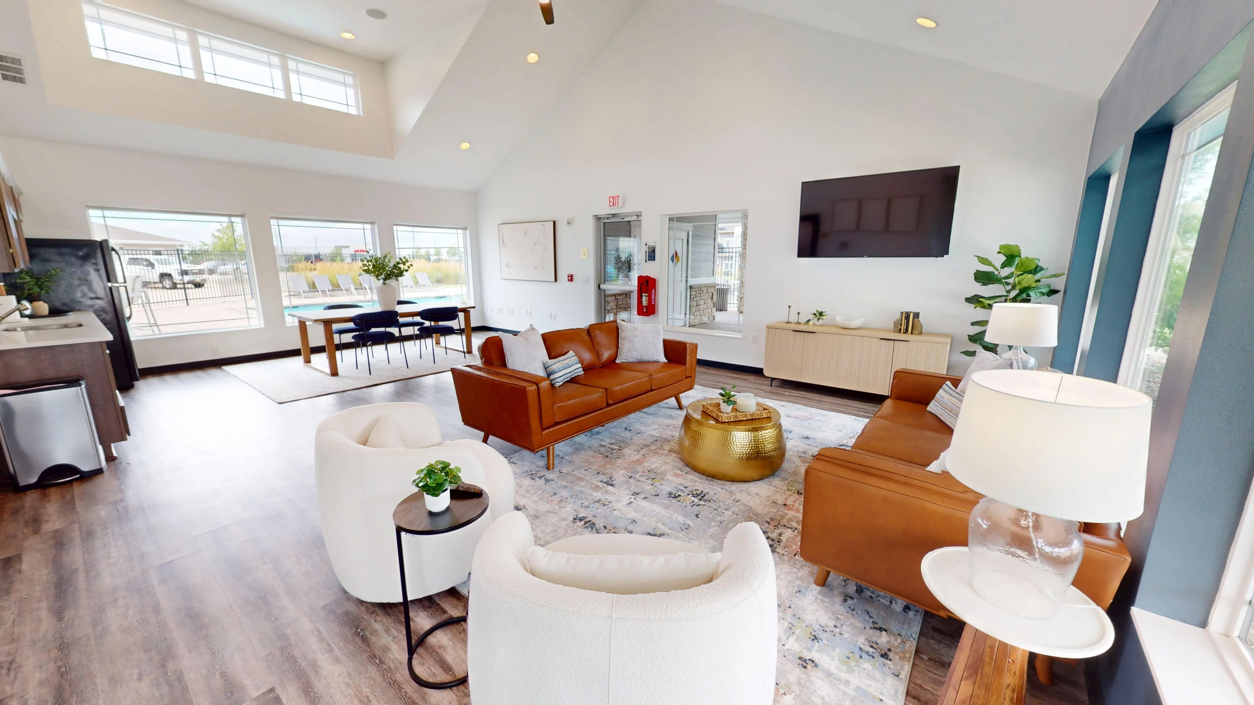 Bright and modern open-concept living area with high ceilings, featuring sleek leather sofas, a stylish rug, and a dining space with large windows overlooking the outdoors.
