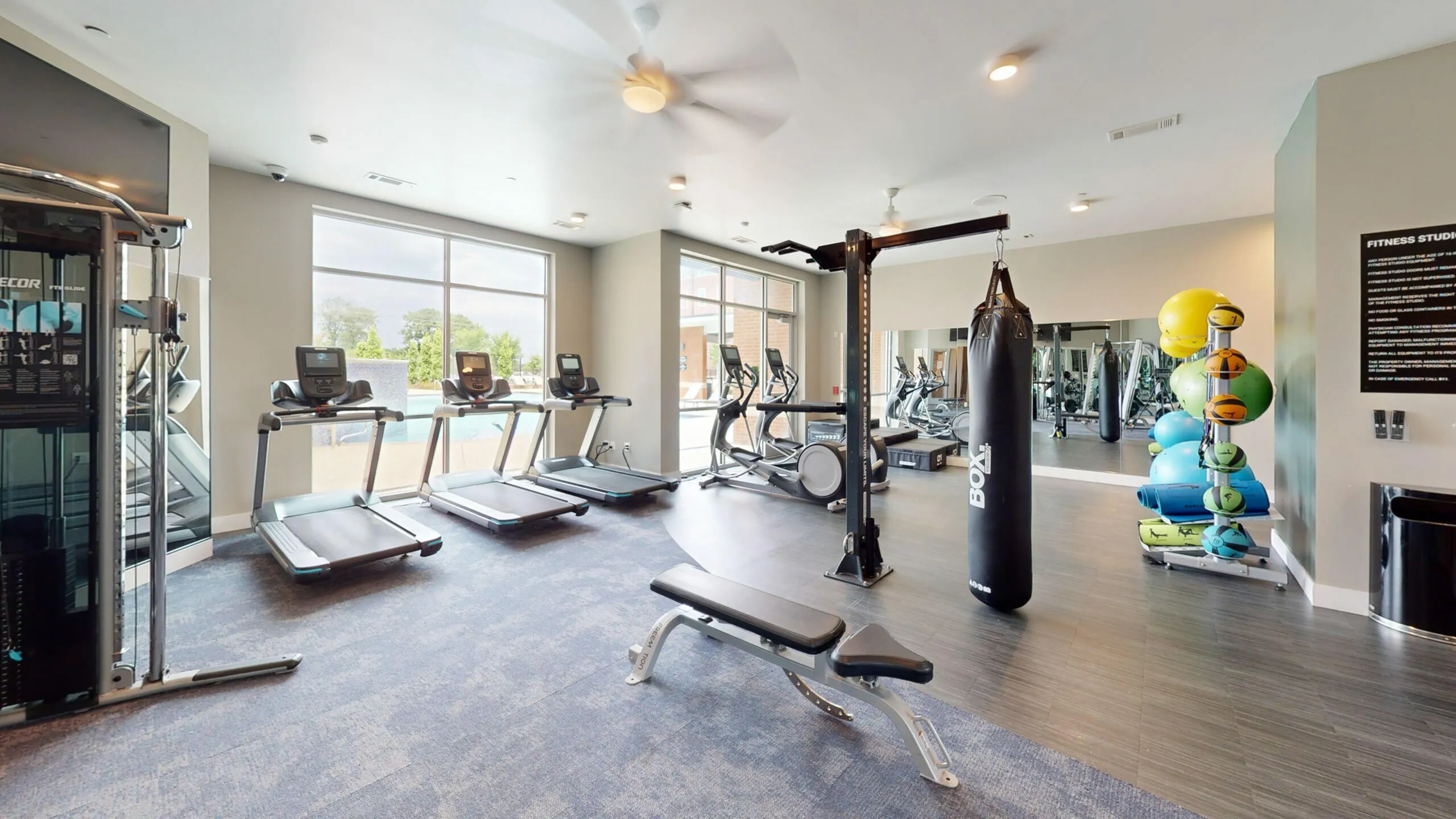 Modern fitness center with state-of-the-art gym equipment, large windows, and a serene outdoor pool view.