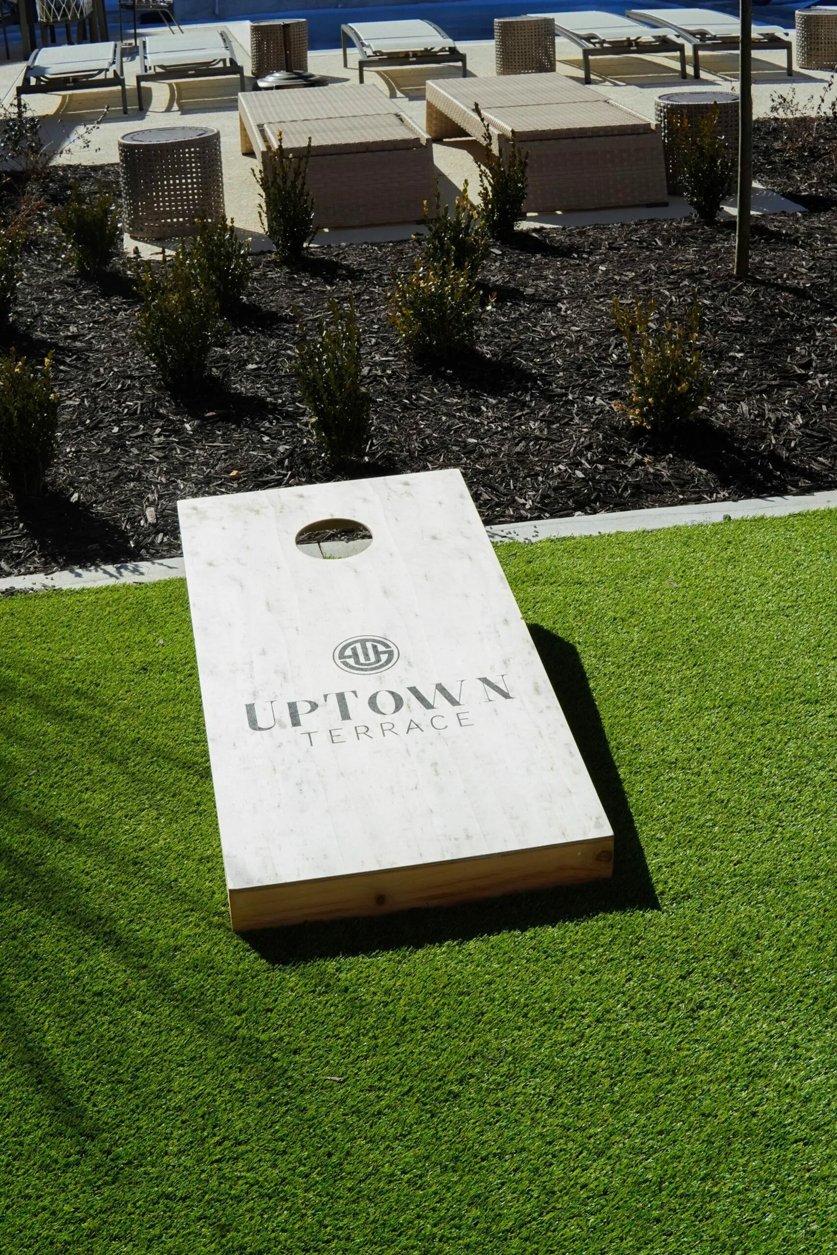Vibrant outdoor area featuring a cornhole game on lush green grass, surrounded by stylish lounge chairs at Uptown Terrace.
