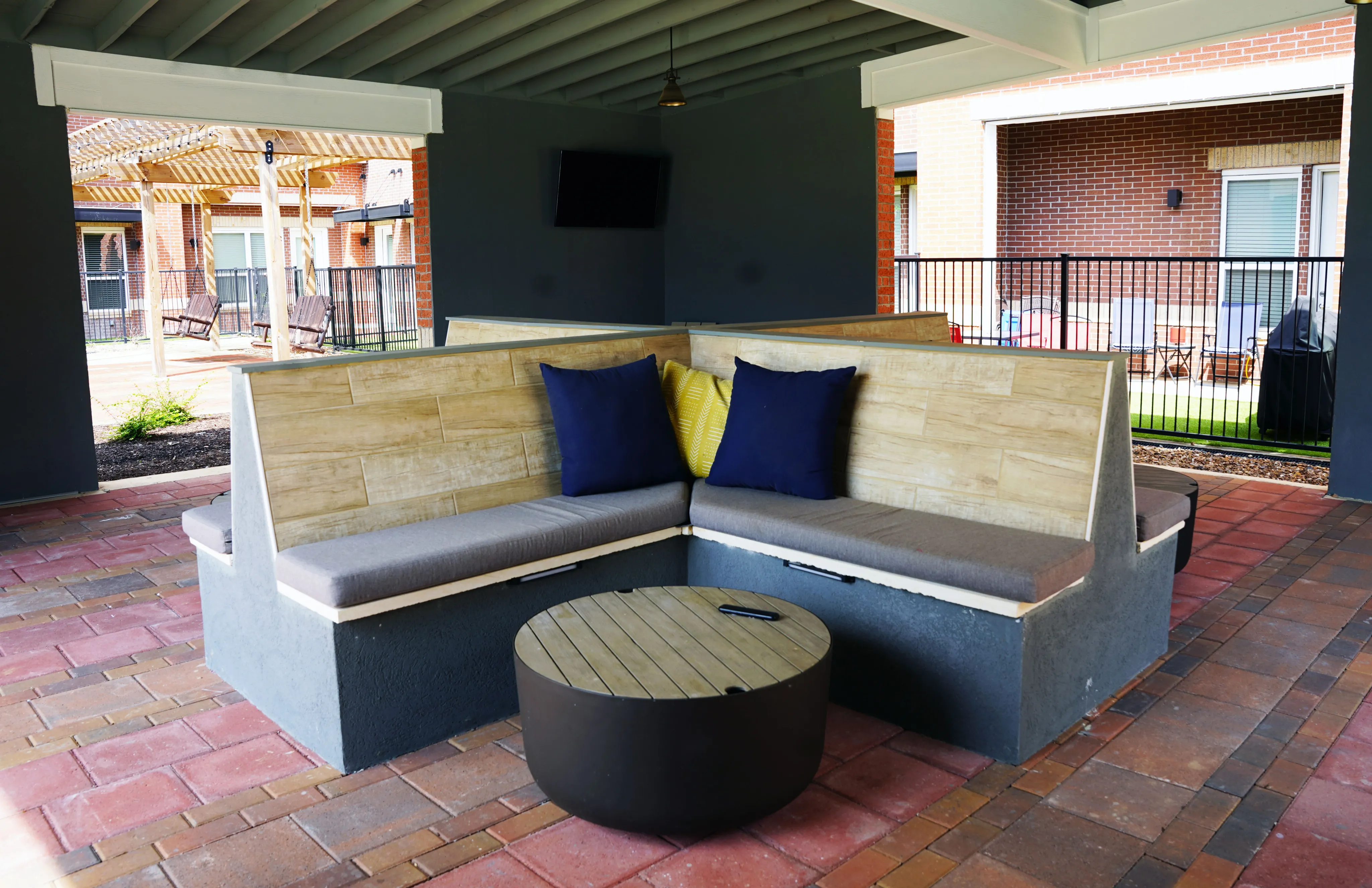 Chic outdoor lounge area featuring a modern L-shaped bench with plush cushions and a round wooden table, perfect for relaxation under a covered patio.