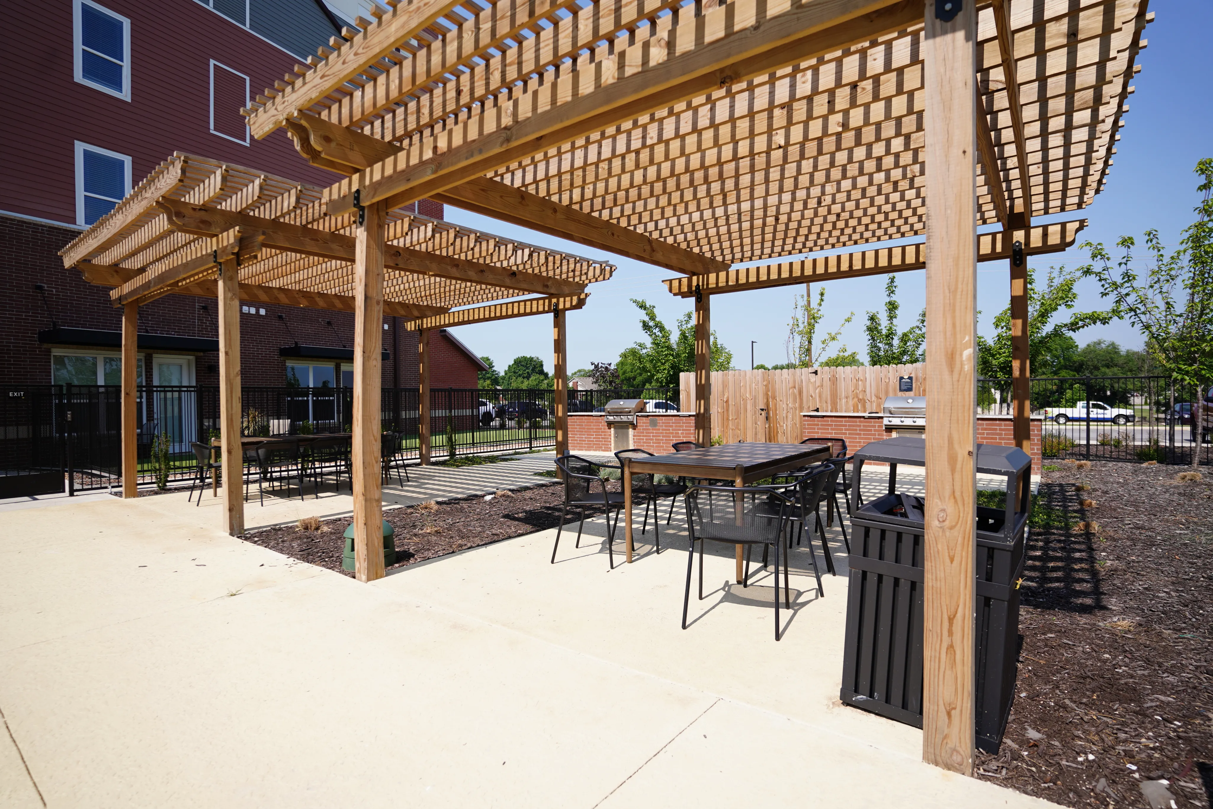 Inviting outdoor patio with wooden pergola, dining tables, and barbecue grills, perfect for entertaining and relaxation.