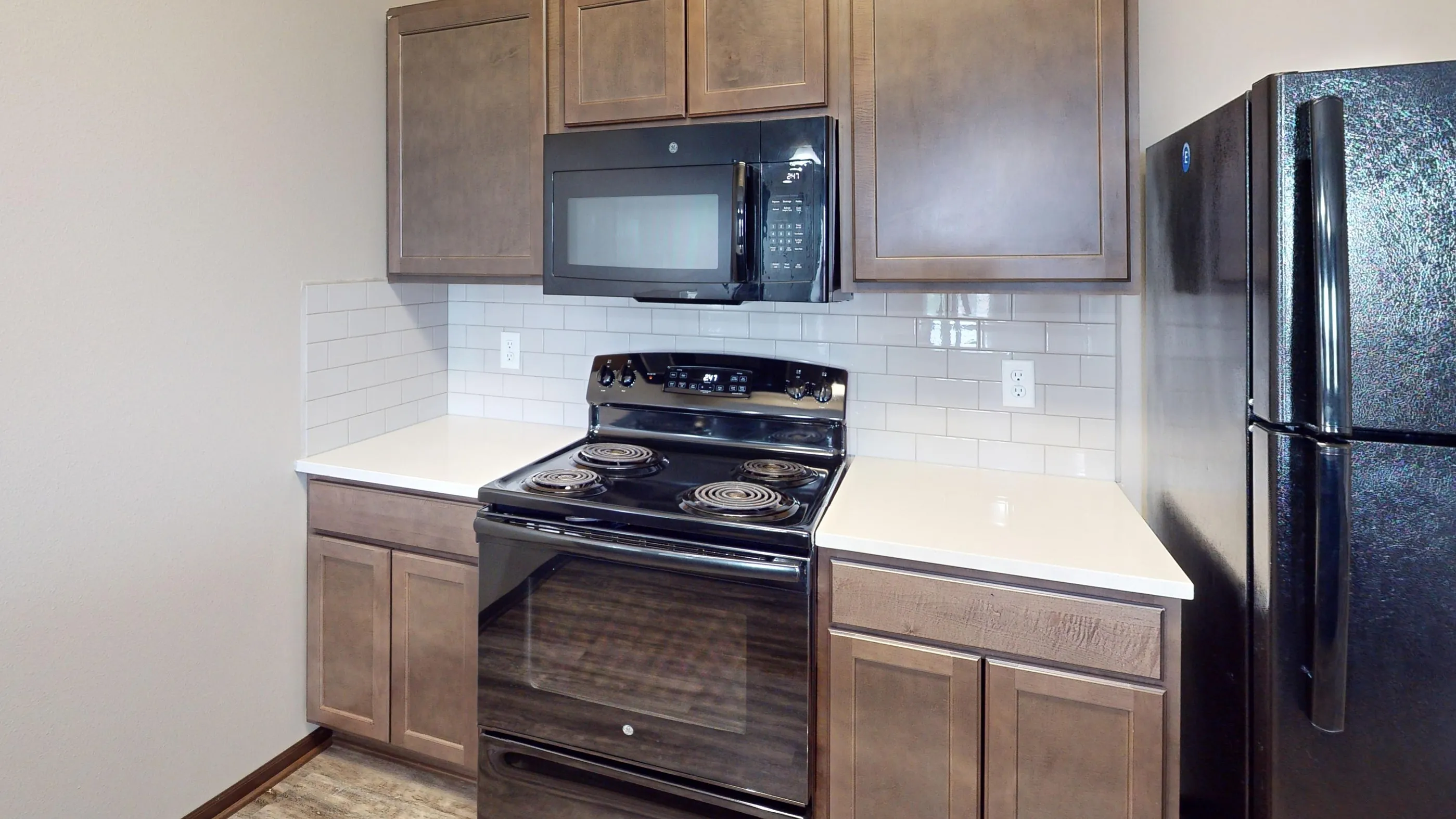 Modern kitchen with sleek black appliances, elegant wood cabinets, and a pristine white tiled backsplash.