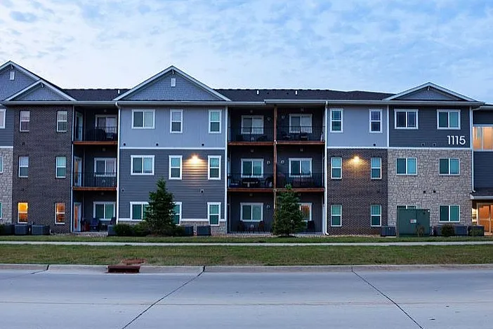 Charming three-story apartment building with modern exterior and private balconies, set against a serene evening sky.