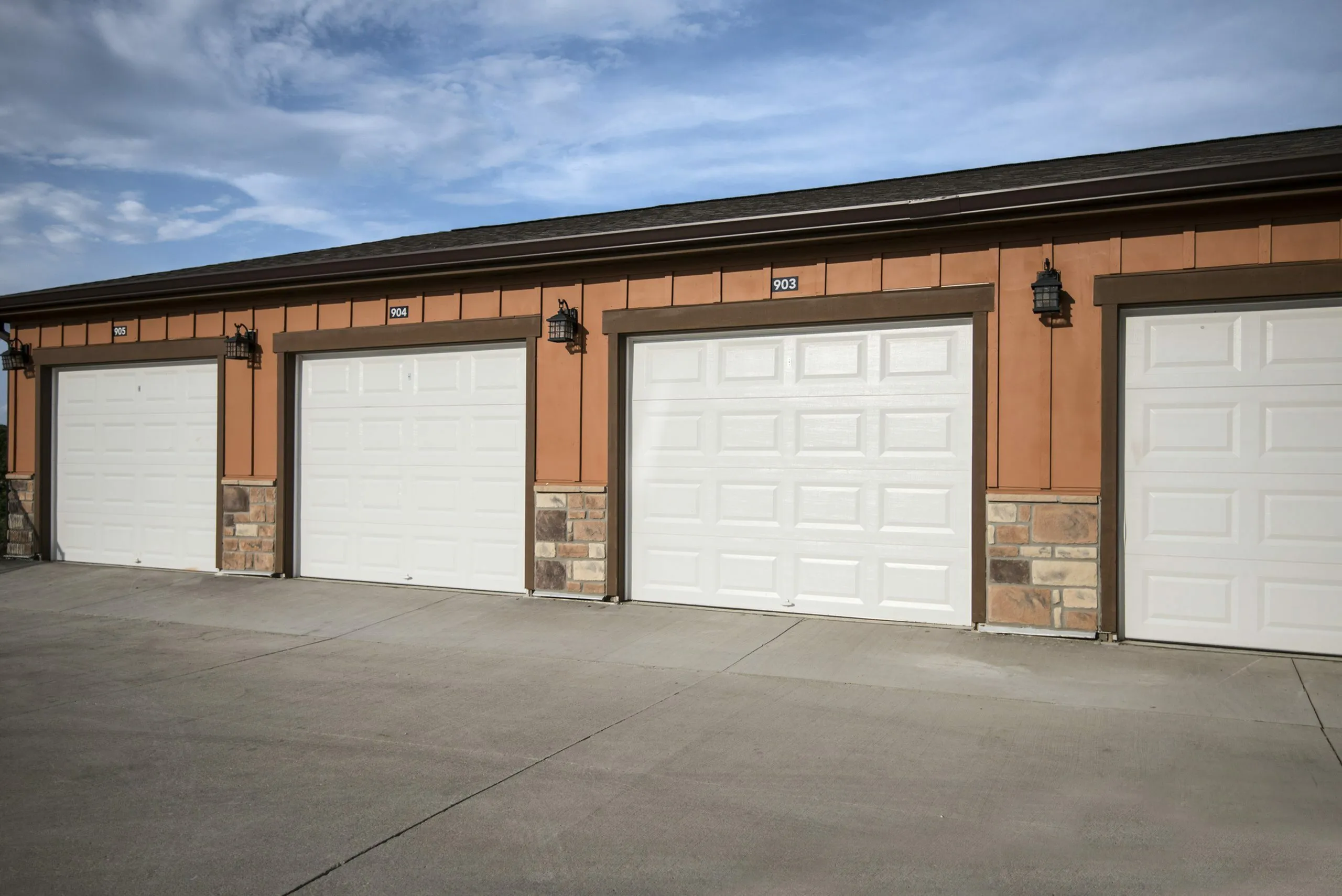 Row of three elegant garages with stylish exterior lighting and textured stone accents under a clear blue sky.
