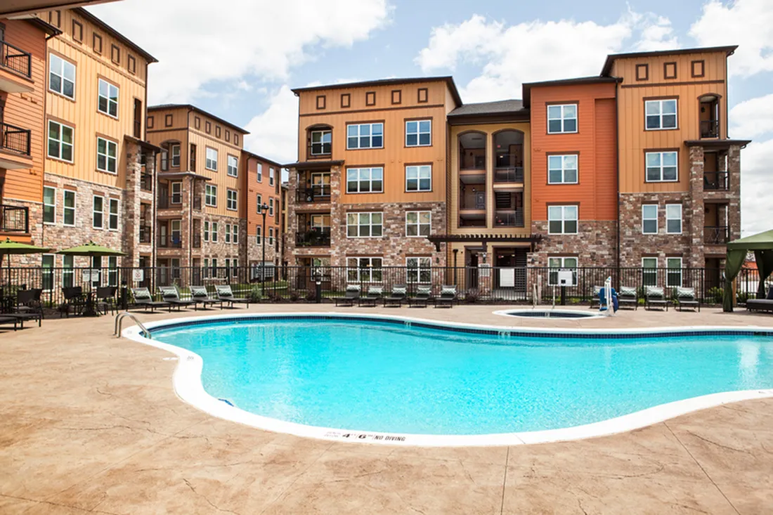 Charming apartment complex with rustic architecture features a sparkling blue pool, perfect for relaxation and leisure.