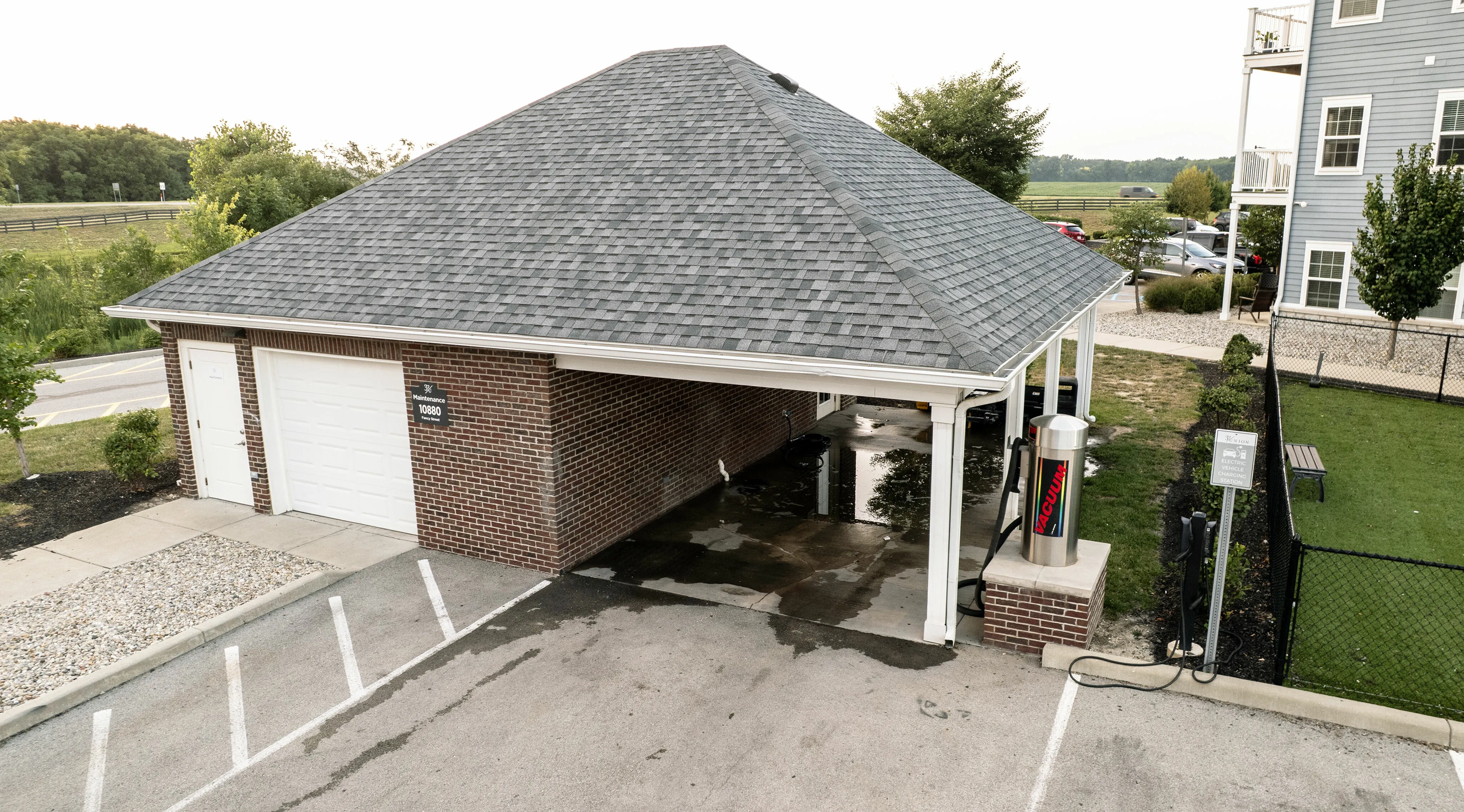 Inviting carport with a stylish grey shingle roof, featuring a modern vacuum station and surrounded by lush greenery. Ideal for keeping your vehicle clean and protected.