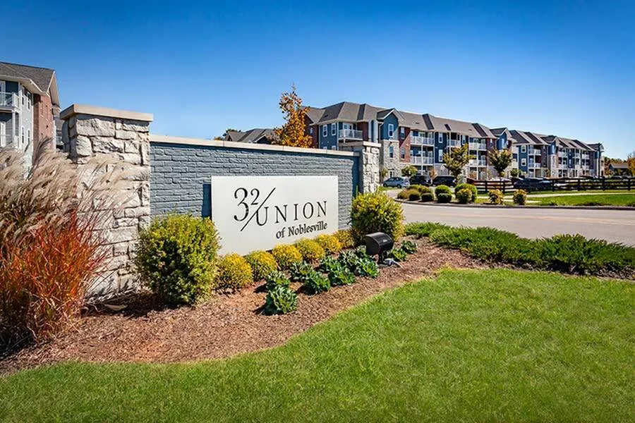 Welcoming entry sign of 32 Union of Noblesville, showcasing stylish apartment buildings and vibrant landscaping under a clear blue sky.