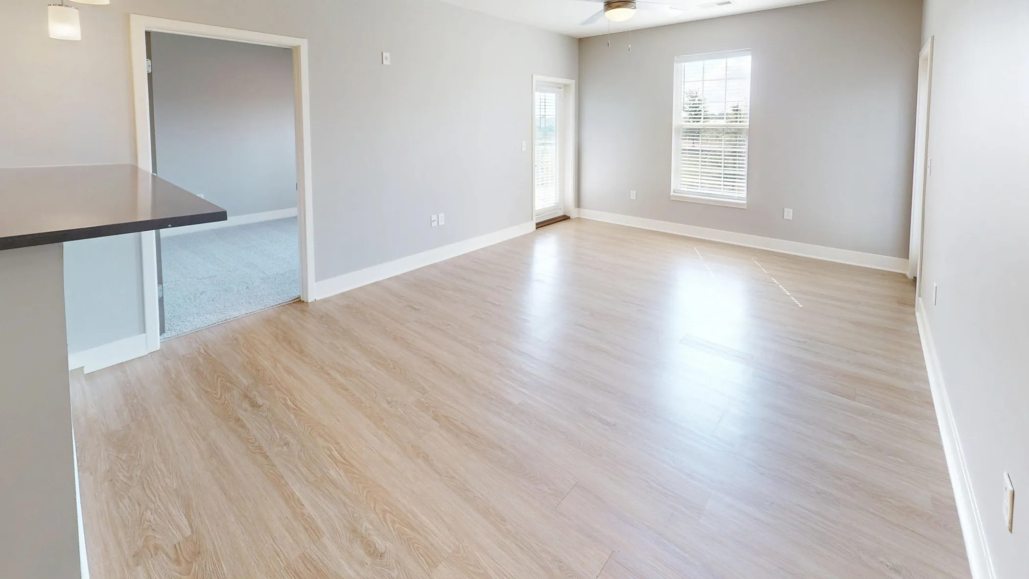 Bright and modern open-plan living area with sleek hardwood floors, a stylish kitchen with white cabinetry, and abundant natural light from large windows.