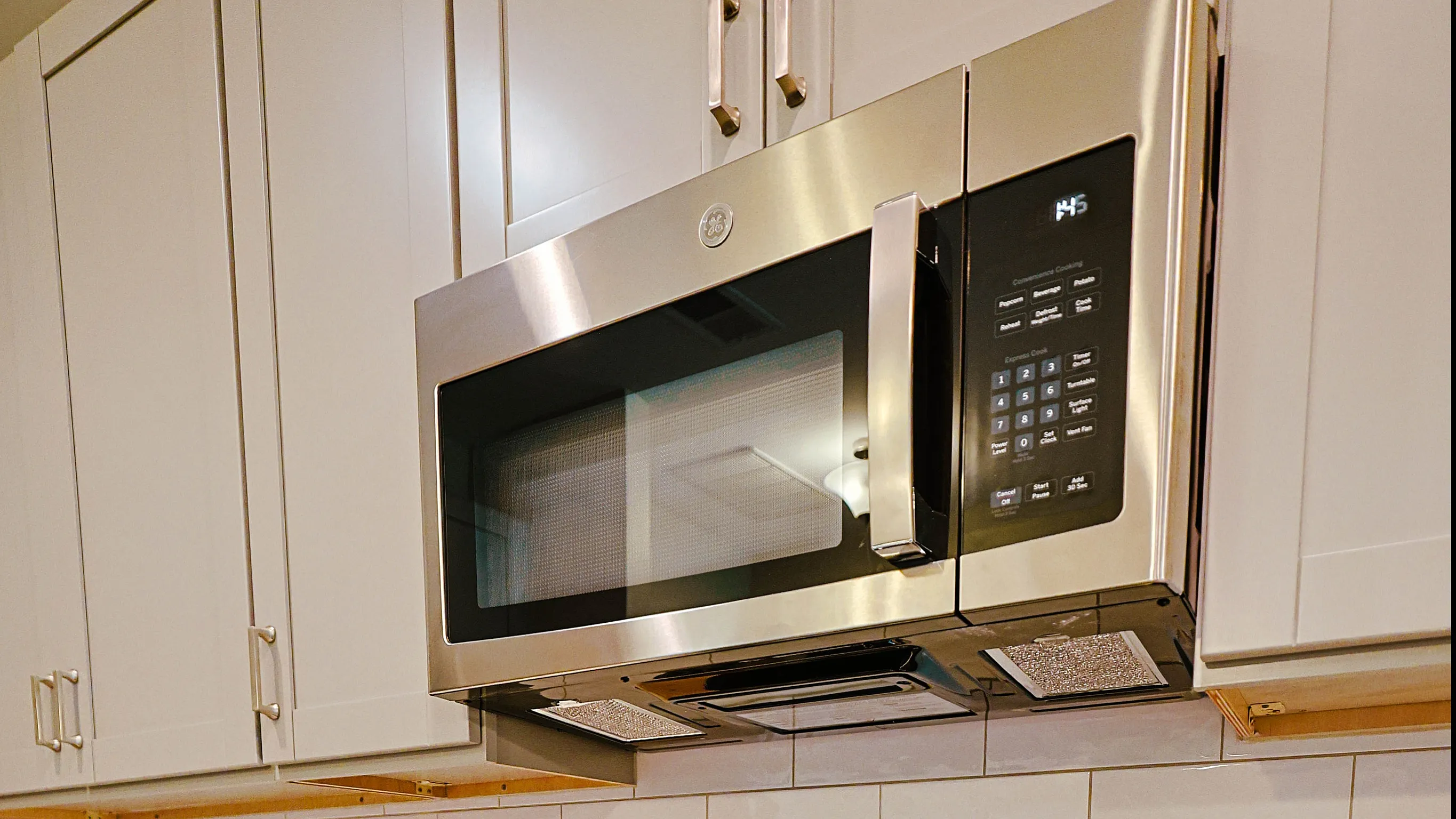Modern kitchen with sleek stainless steel appliances, including a microwave and oven, complemented by elegant white cabinetry and subway tile backsplash.