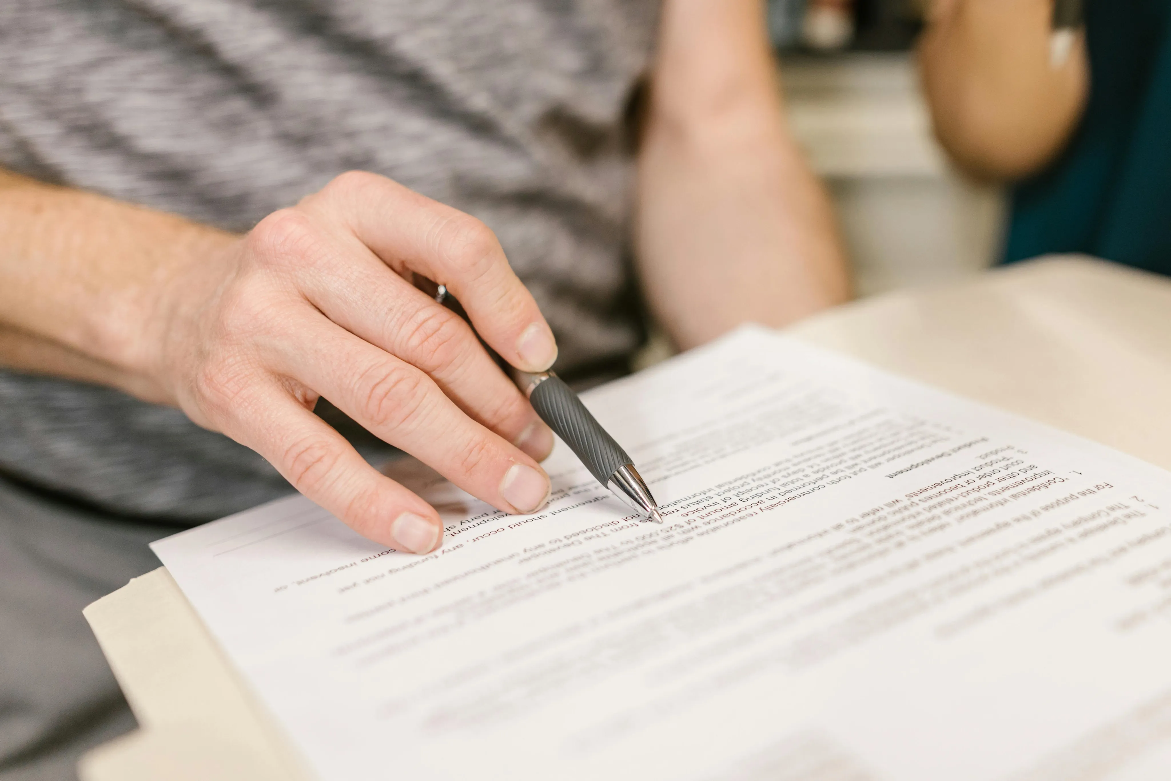 Close-up of a hand holding a pen, poised over a detailed document, illustrating precision and attention to detail in paperwork.