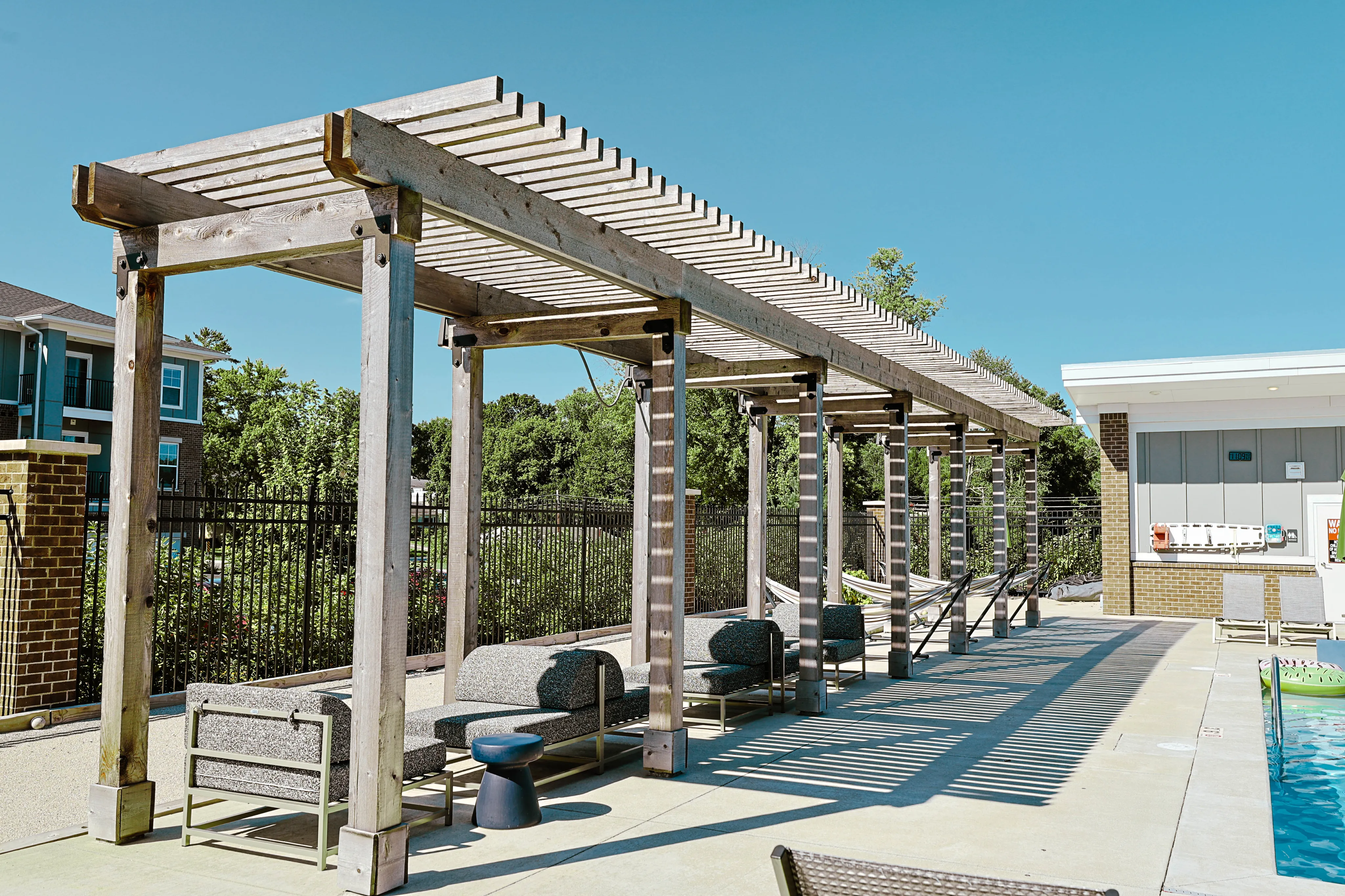 Inviting outdoor space featuring a stylish wooden pergola with comfortable seating and hammock areas, set beside a refreshing pool.