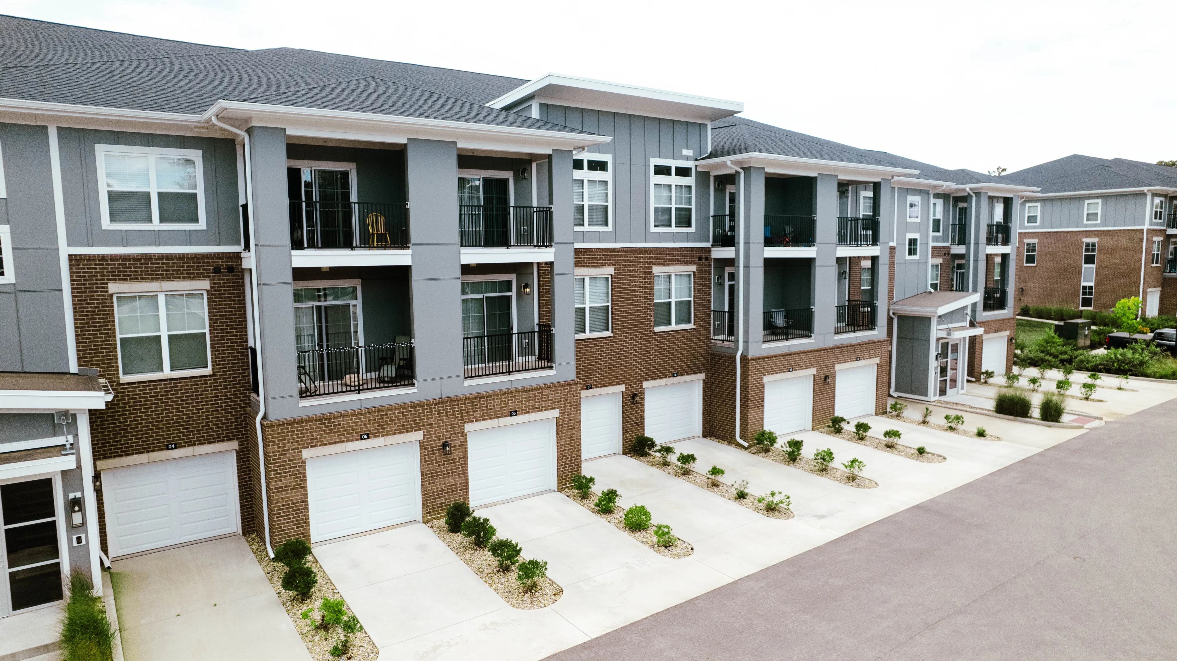 Modern apartment complex with sleek architectural design, featuring balconies and attached garages, set in a well-maintained community.