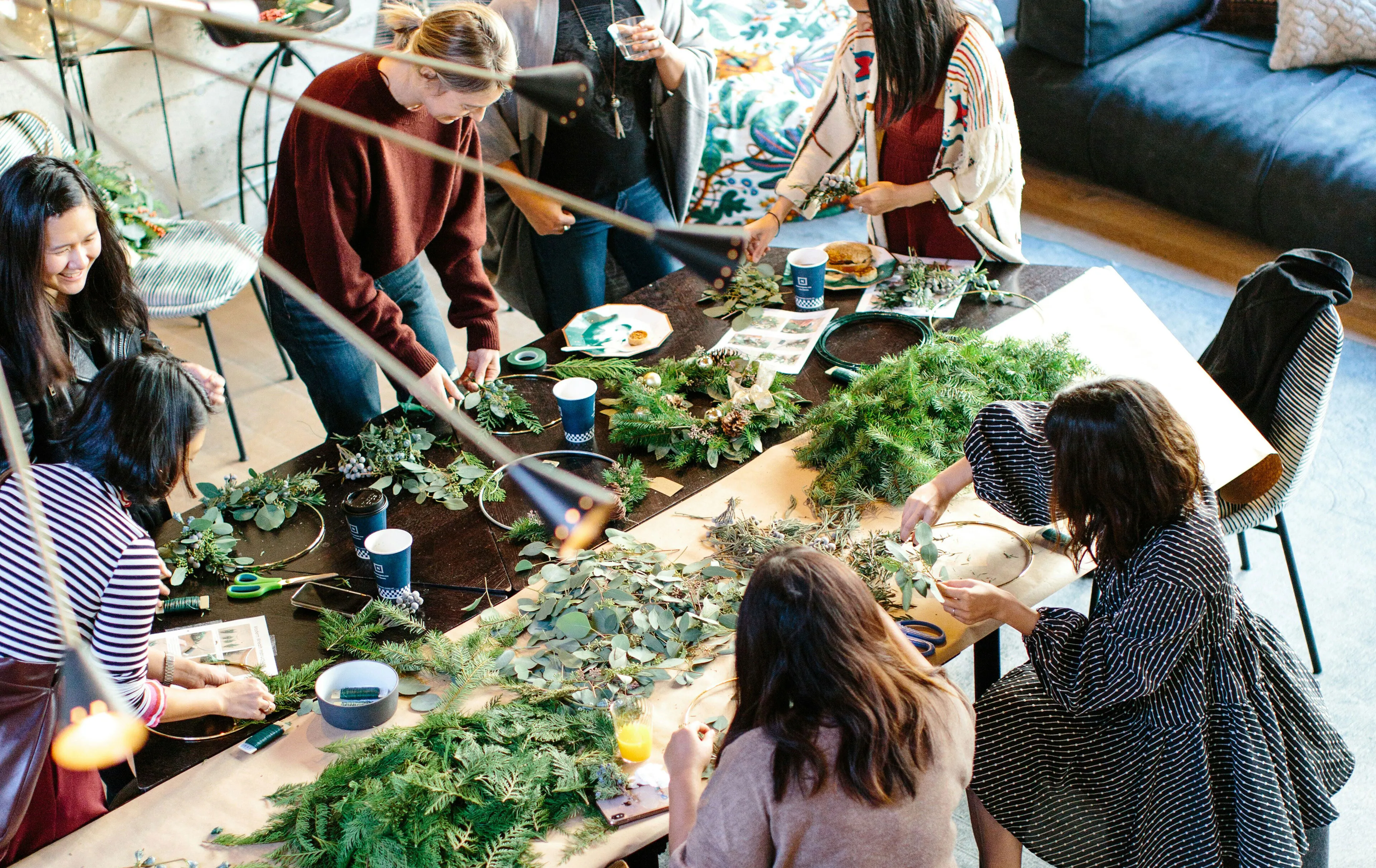 Vibrant social gathering with people creating floral arrangements around a cozy table, surrounded by creative decor.