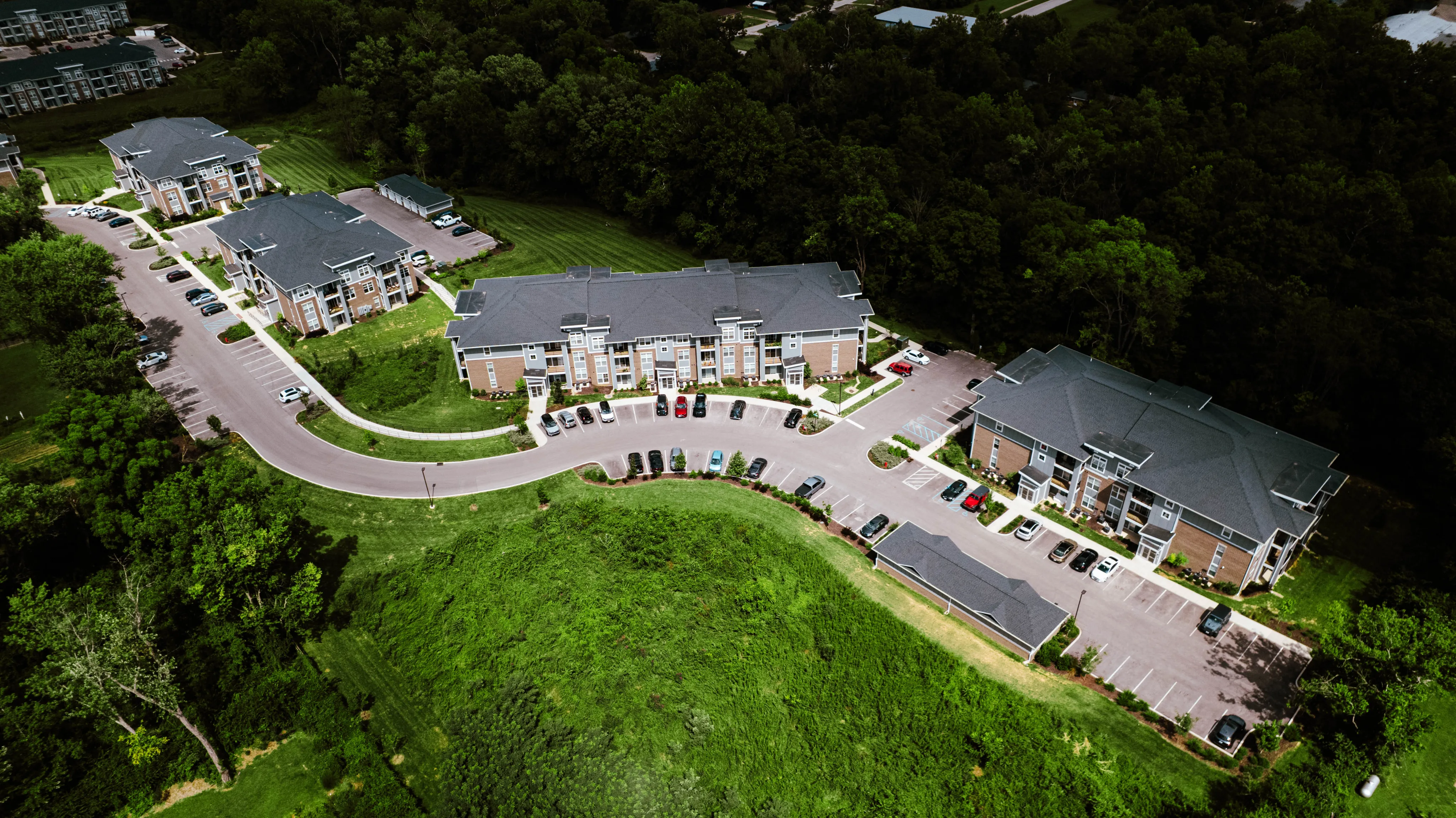 Stunning aerial view of modern apartment complex surrounded by lush greenery, featuring ample parking and well-maintained pathways for a serene living experience.