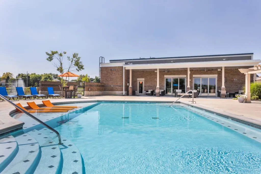 Luxurious apartment complex showcasing a sparkling outdoor swimming pool with elegant lounge chairs and a modern clubhouse in the background.