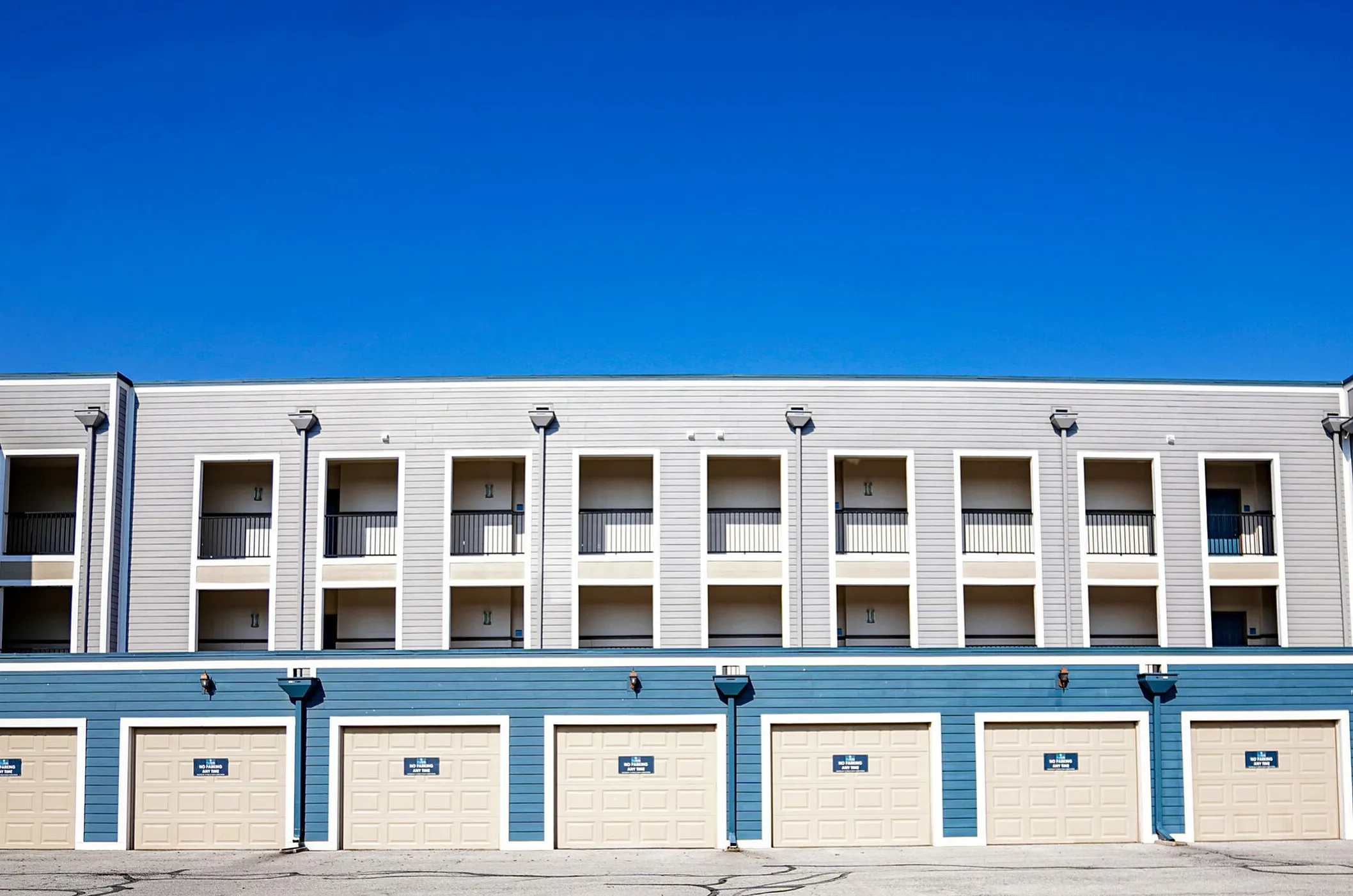 Modern apartment complex exterior with multiple balconies, under clear blue skies, featuring convenient ground-level garages.