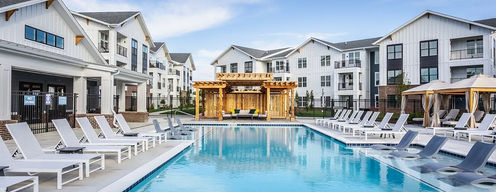 Luxurious apartment complex featuring a stunning outdoor pool area with modern lounge chairs and a beautiful pergola, perfect for relaxation and entertainment.
