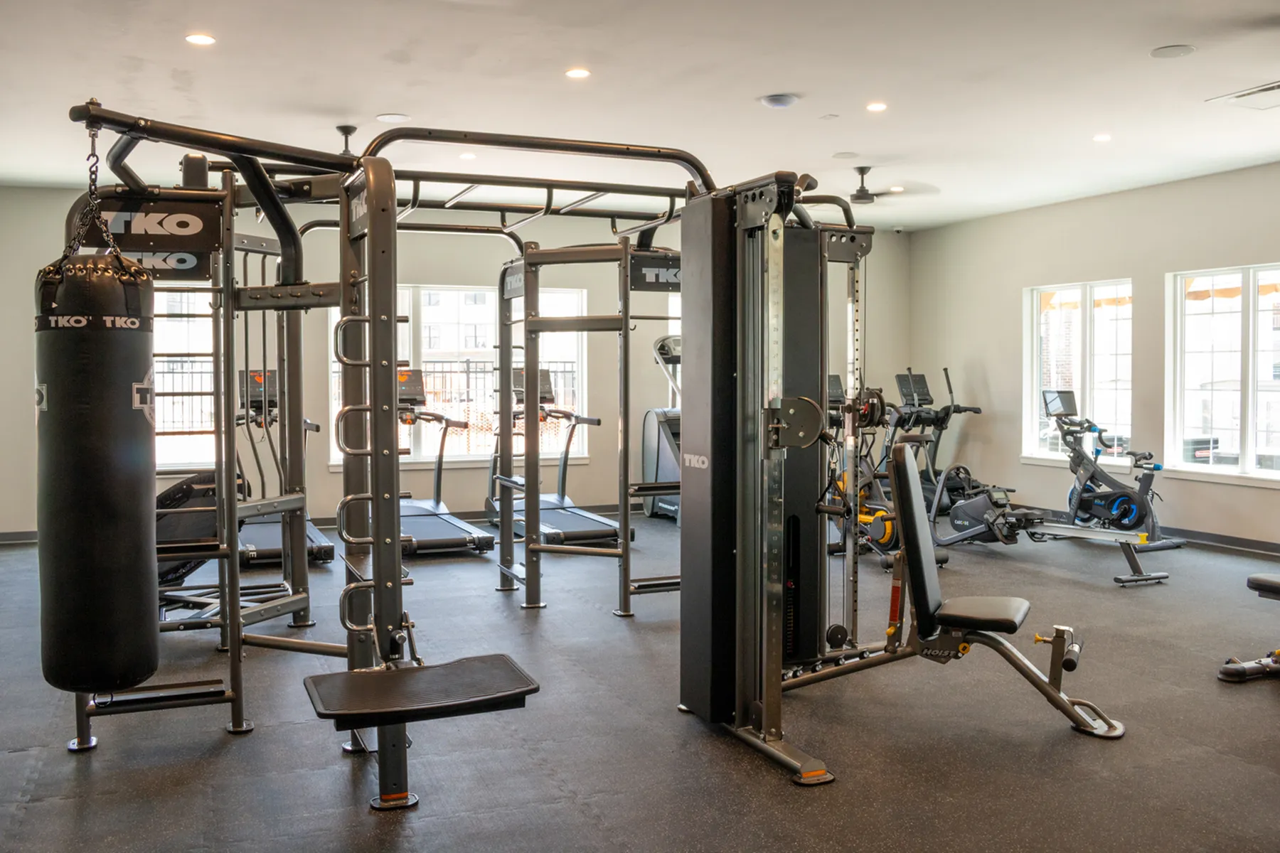 Modern fitness center with state-of-the-art exercise equipment, treadmills, weight machines, and a punching bag in a bright, airy space.