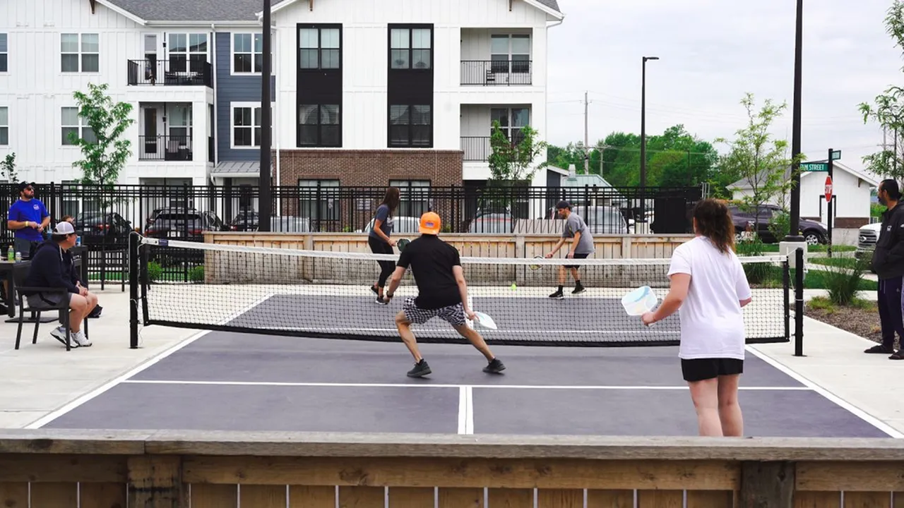 Dynamic pickleball game in vibrant apartment community setting with modern buildings in the background.