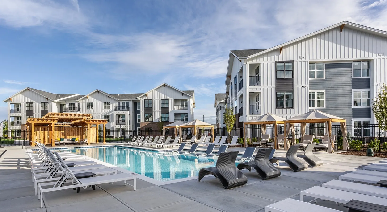 Modern apartment complex with a luxurious outdoor pool, stylish lounge chairs, and elegant cabanas under a clear blue sky.