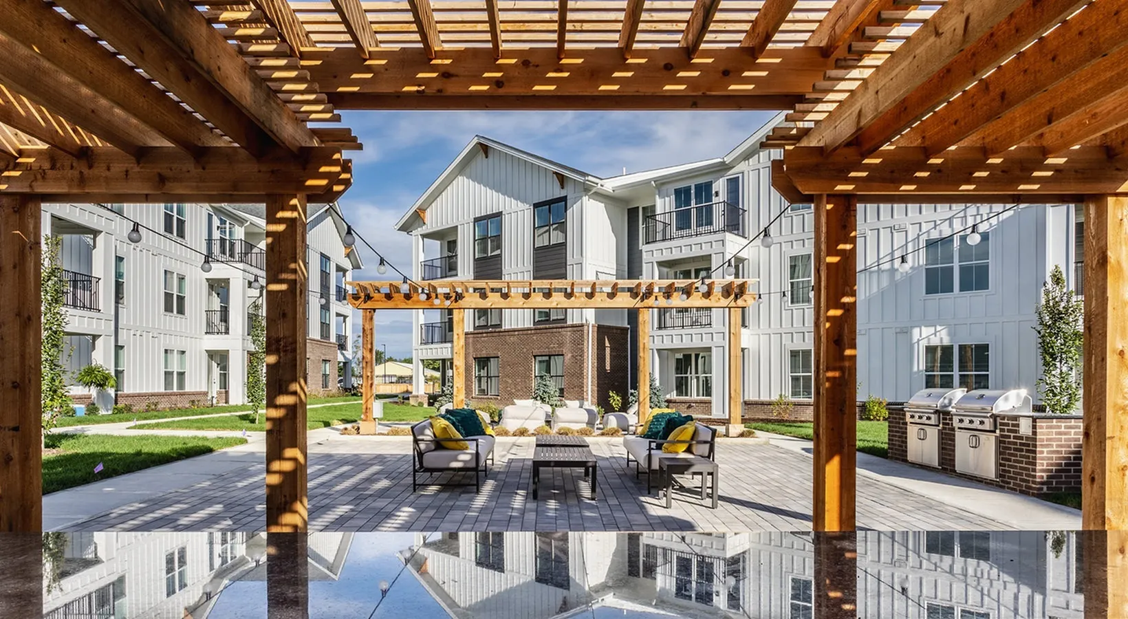Inviting outdoor patio at modern apartment complex with cozy seating, stylish pergola, and barbecue grills for community gatherings.