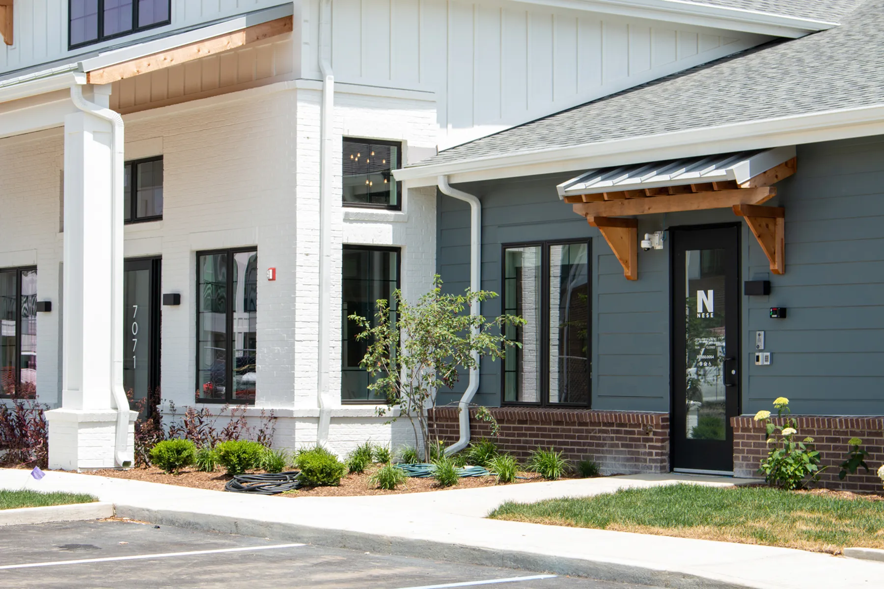 Charming modern residence exterior showcasing a blend of white brick and blue siding with stylish windows and lush landscaping.
