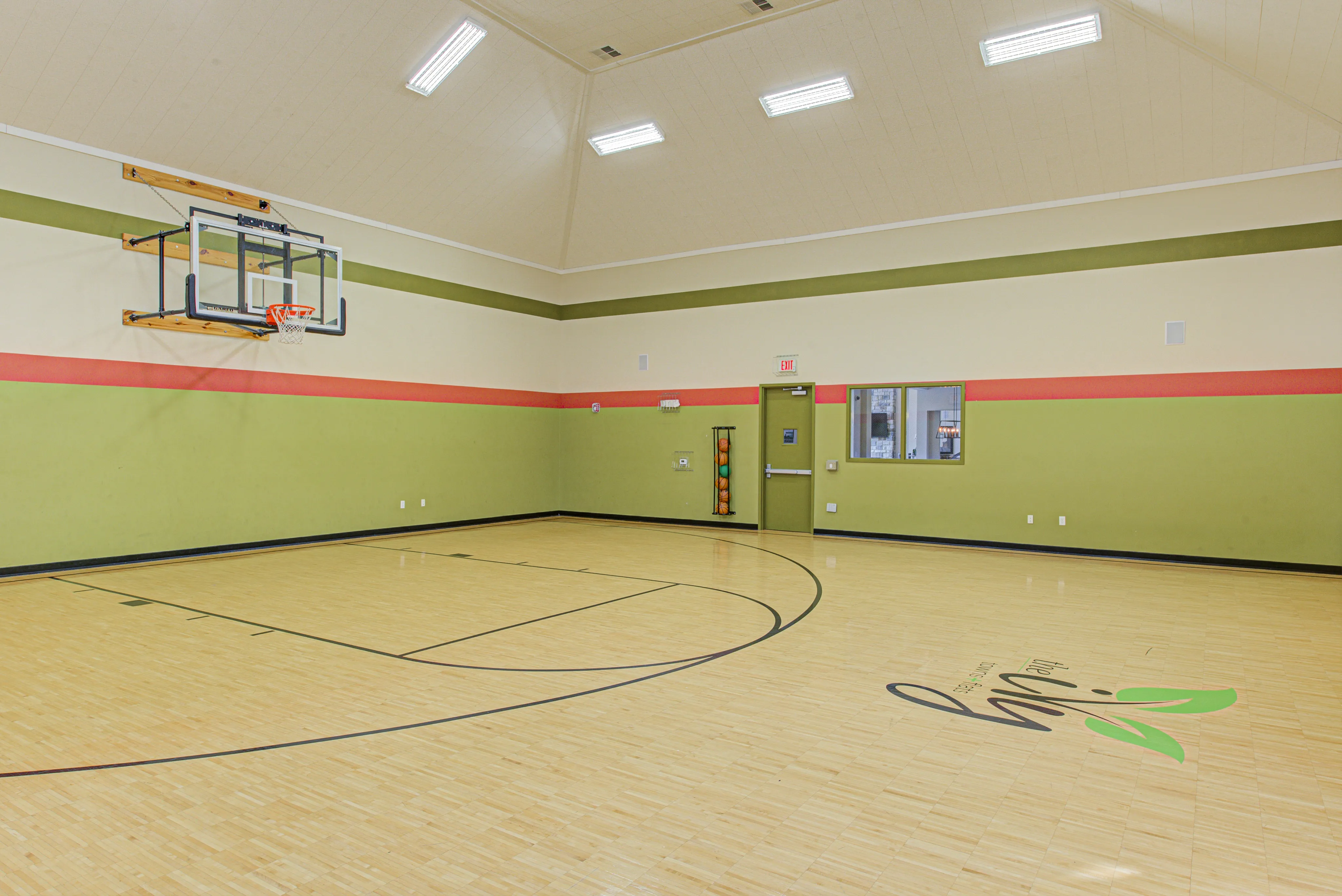 Spacious indoor basketball court with modern design, featuring polished hardwood floors and vibrant wall colors.