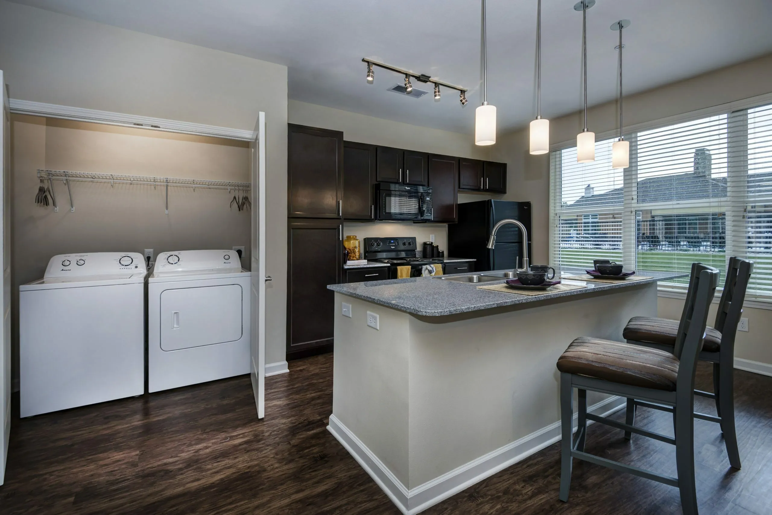 Modern kitchen with sleek dark cabinets, stylish pendant lighting, and an inviting breakfast bar, paired with a convenient in-unit laundry area.