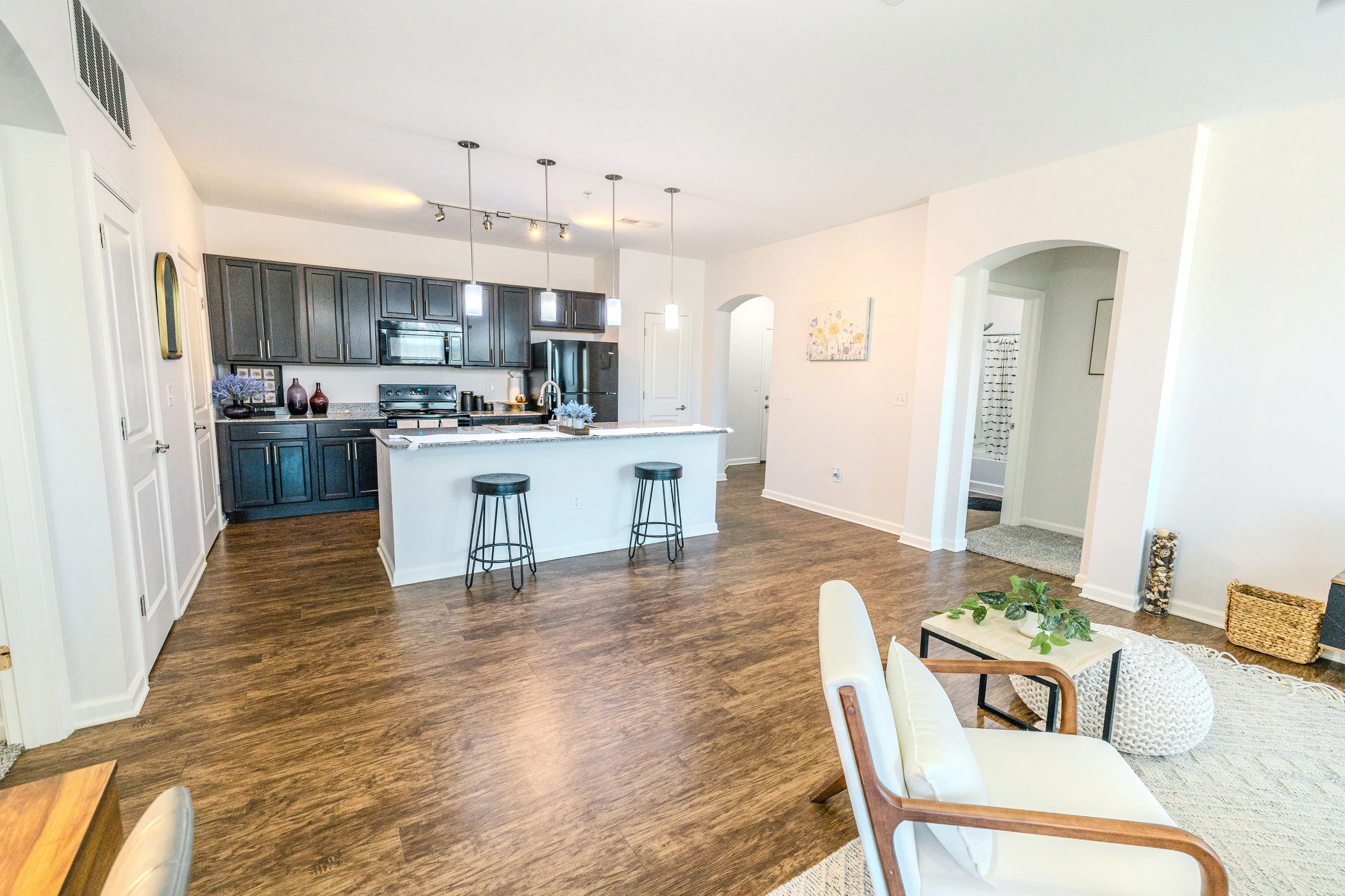 Chic open-concept living area with a modern kitchen, featuring sleek dark cabinetry, stylish pendant lighting, and cozy seating accents on rich wood flooring.