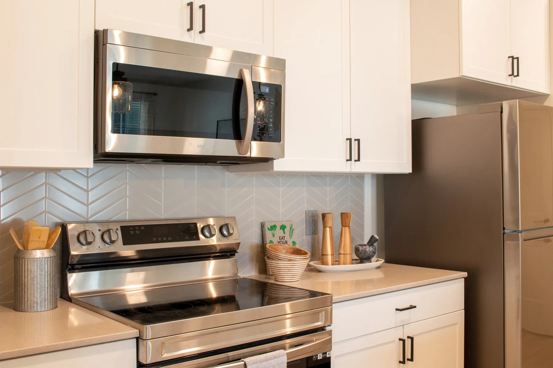 Modern kitchen with sleek stainless-steel appliances, elegant white cabinetry, and a stylish herringbone tile backsplash.