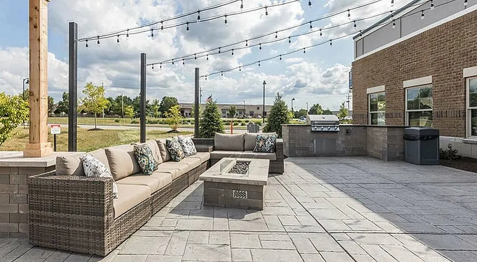 Charming outdoor patio featuring stylish wicker seating, string lights, and a modern barbecue area, perfect for entertaining.
