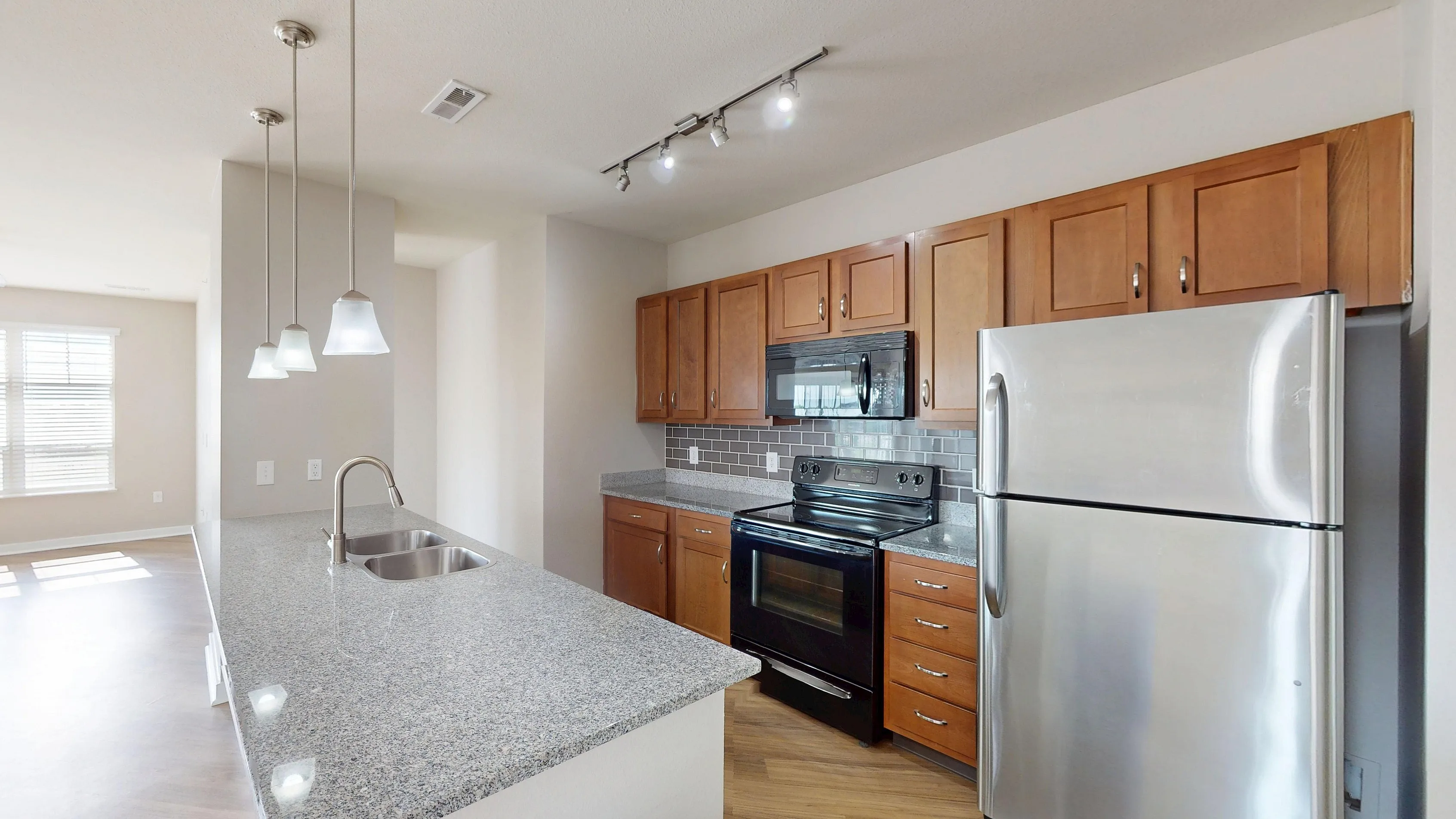 Modern open-concept kitchen with sleek granite countertops, stainless steel appliances, and warm wooden cabinetry, overlooking a bright and airy living space with large windows.