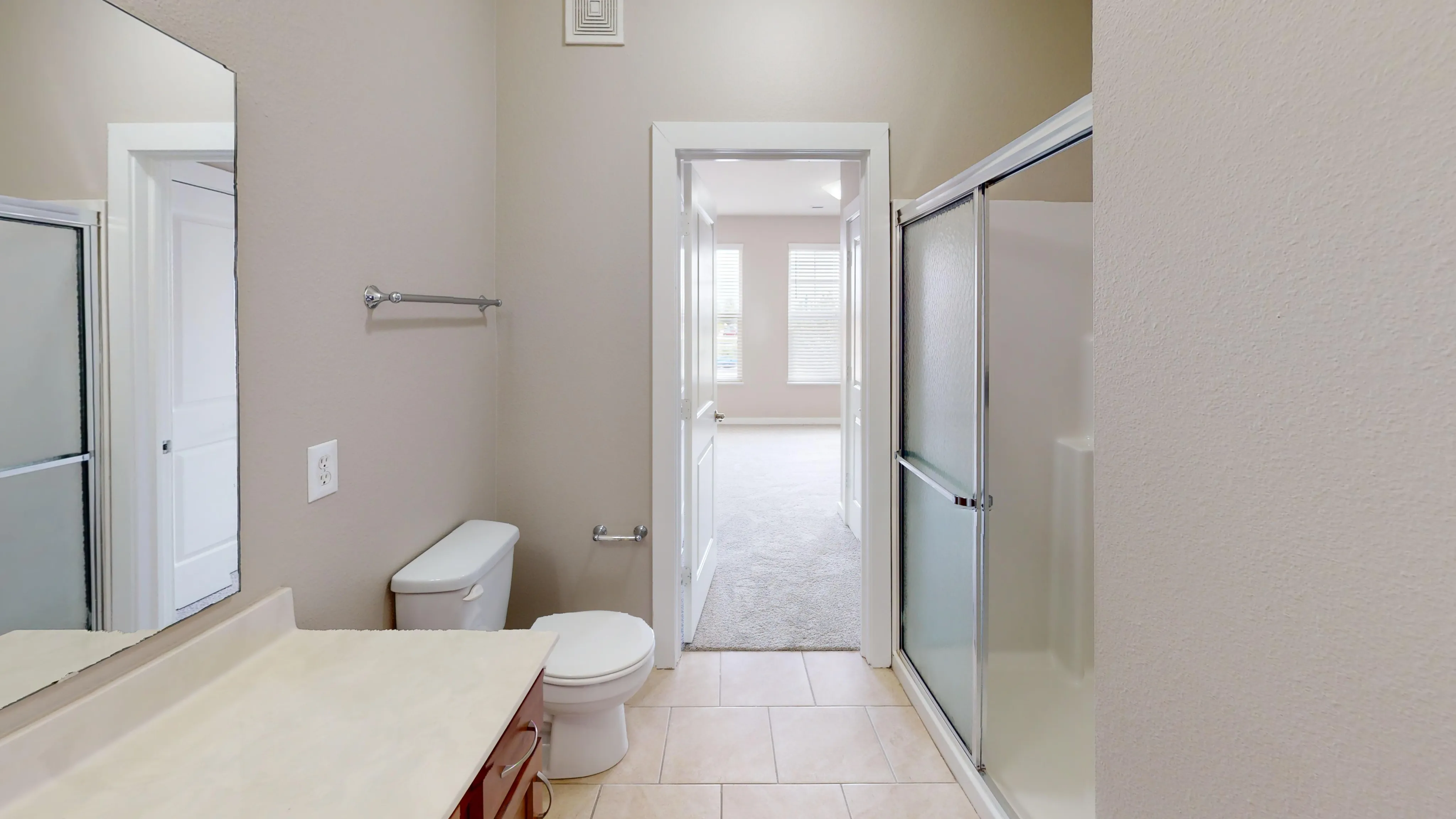 Elegant bathroom with modern shower, sleek sink, and open doorway leading to a bright, spacious room with large windows.