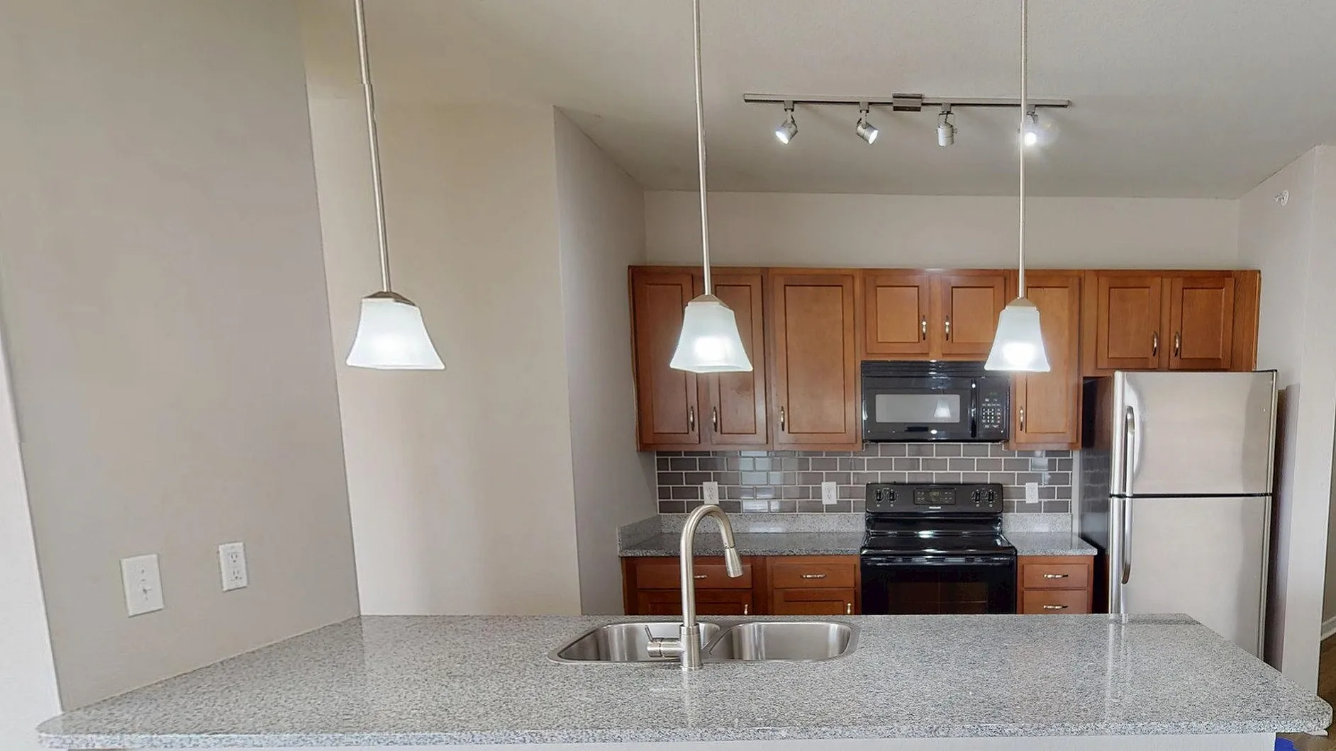 Modern kitchen with sleek granite countertops, wooden cabinetry, stainless steel appliances, and stylish pendant lighting, featuring open layout and wood flooring.