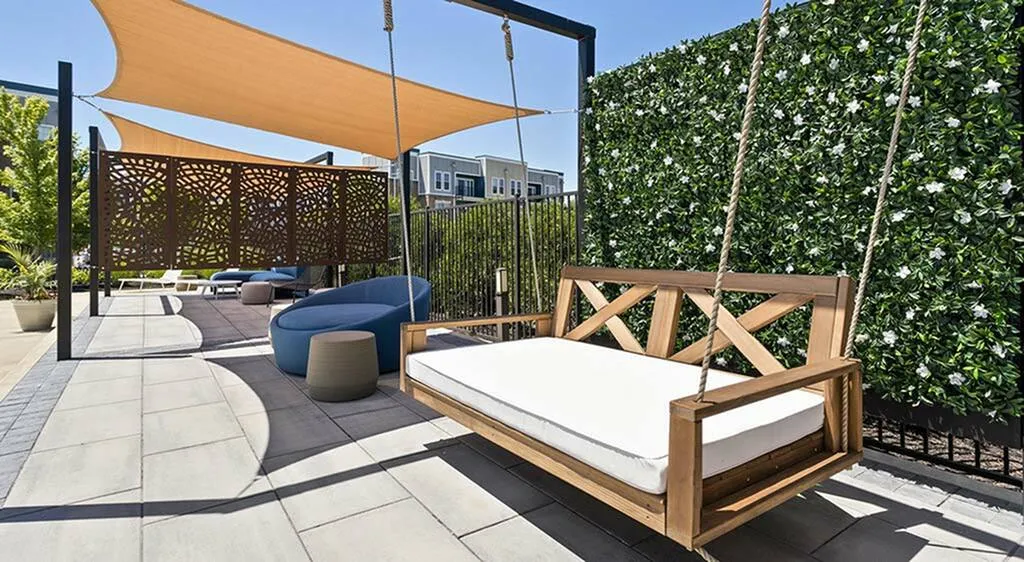 Modern outdoor patio featuring a chic wooden swing, cozy seating areas, and stylish shade sails, perfect for relaxation and entertaining.