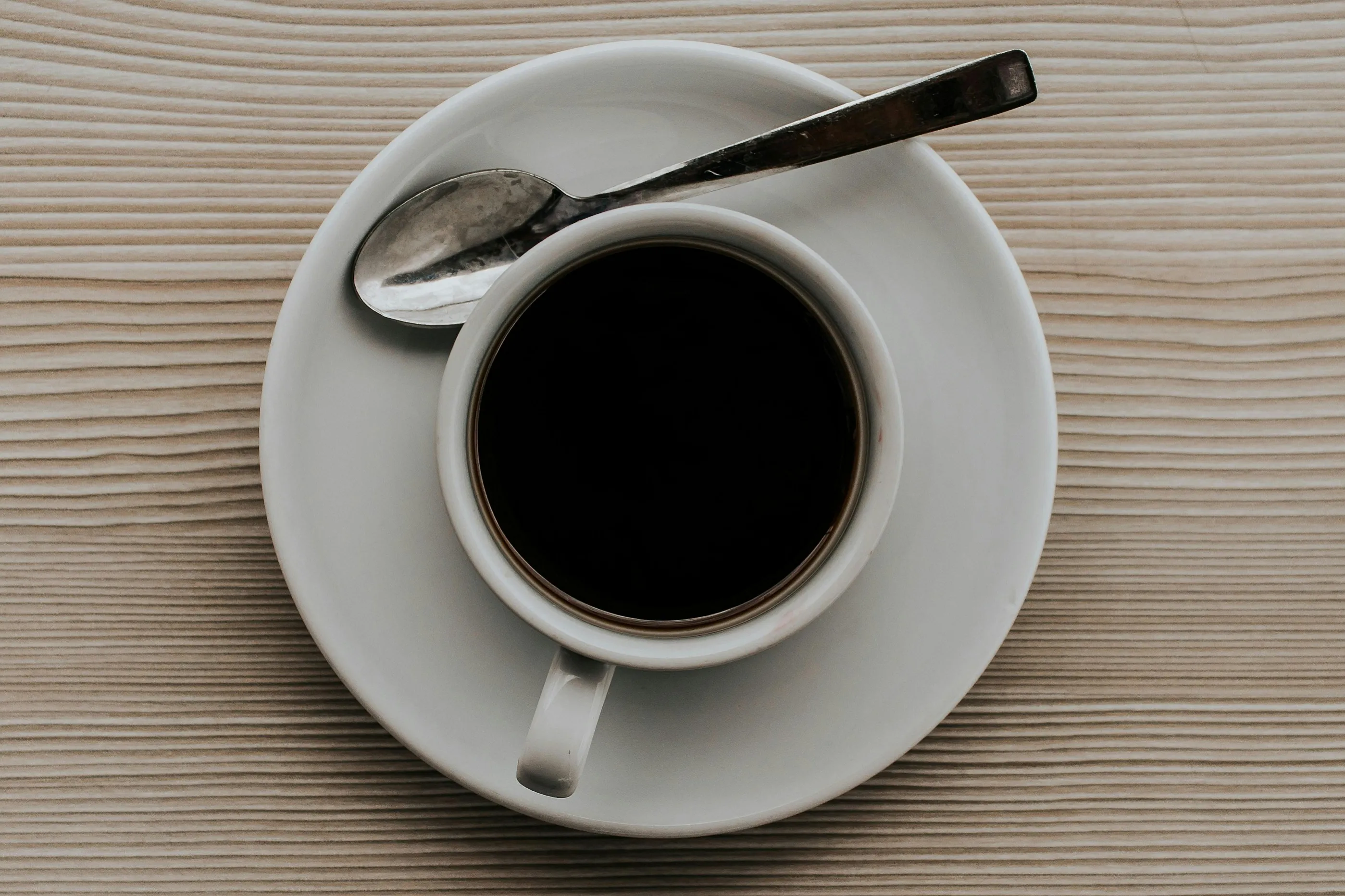 Elegant cup of black coffee with a spoon on a chic wooden table, creating a cozy and inviting atmosphere.